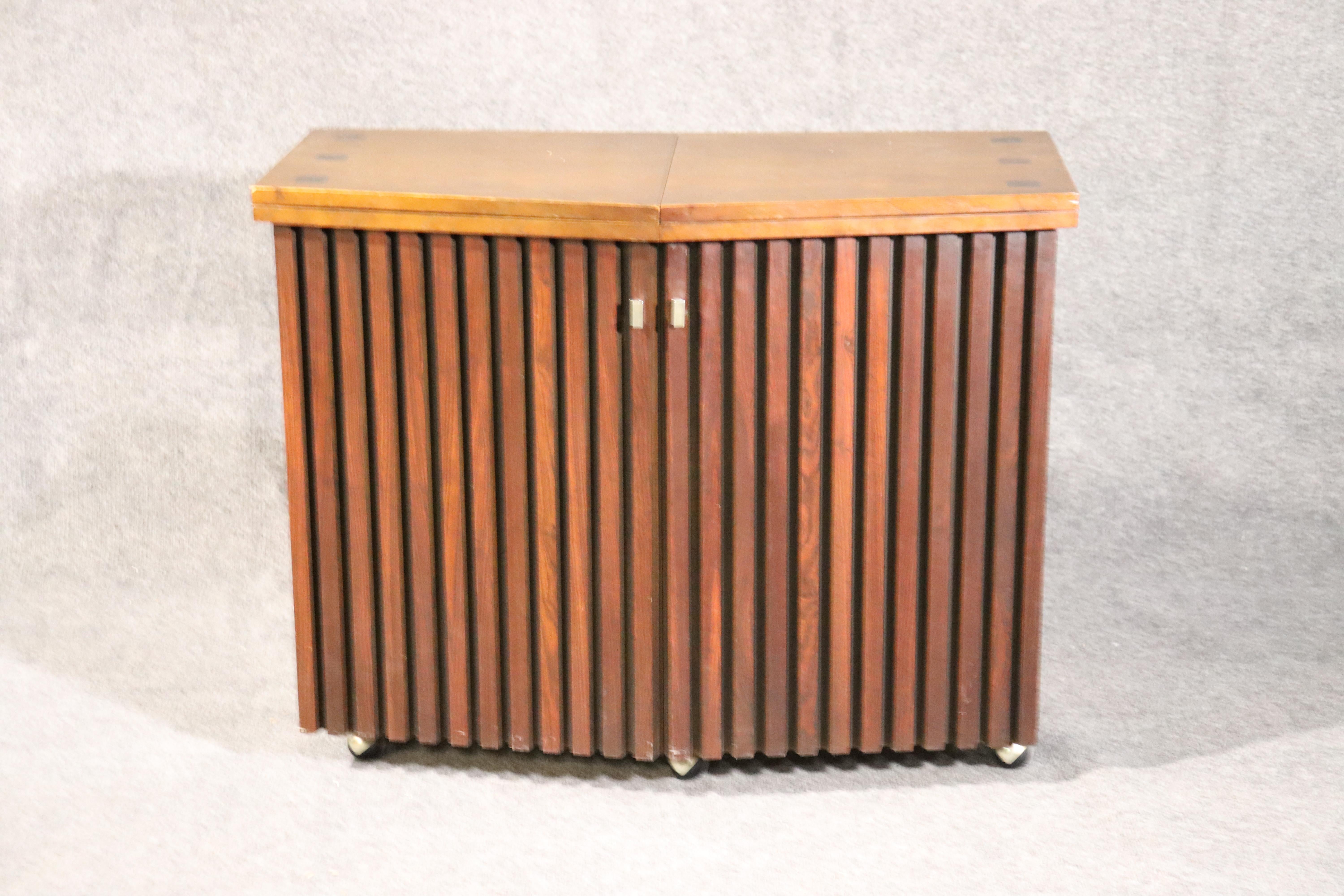 This is a very unique piece by Lane designed in the Mid-Century Modern style. The bar is perfect for use as a buffet or dry bar and is rosewood and walnut. It measures 38 wide x 30 tall x 19 inches deep and when opened its 76 long.