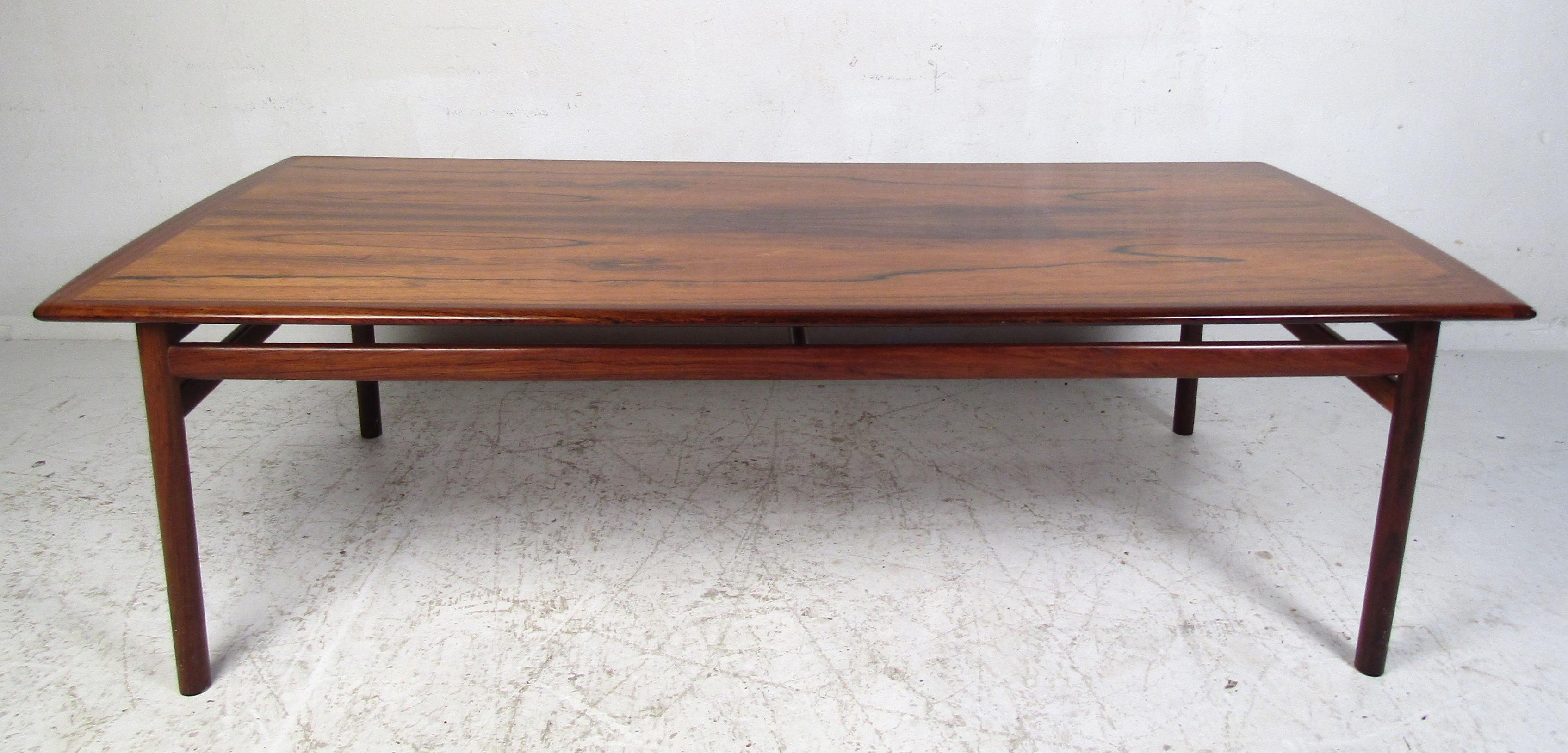 Elegant Danish modern rosewood coffee table with beautiful woodgrain throughout. This vintage rectangular coffee table boasts cylindrical legs connected by stretchers ensuring maximum sturdiness. The perfect addition to any home, business, or