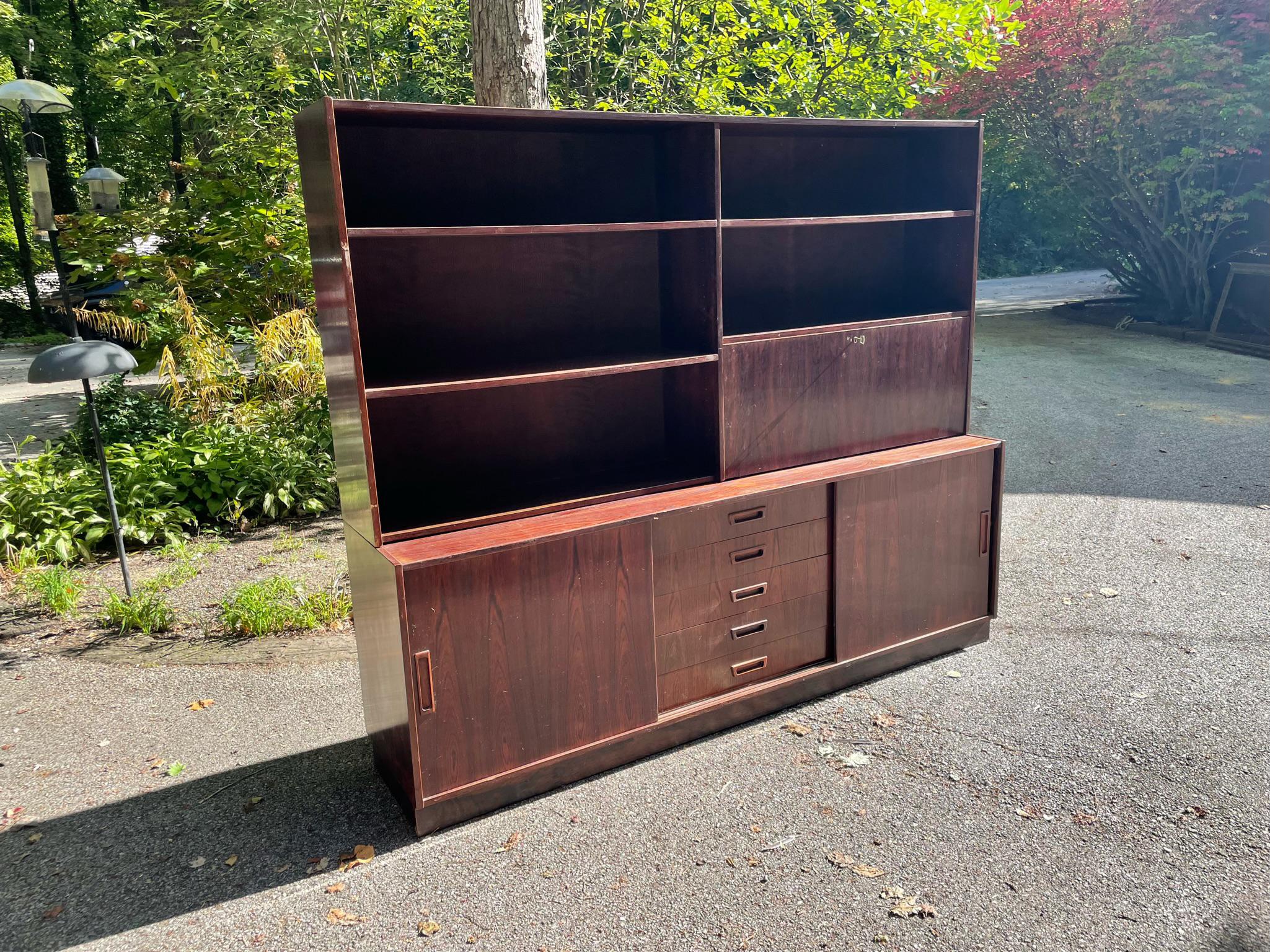 Vintage Danish modern rosewood credenza with removable shelving unit. Absolutely stunning rosewood wood grain. Fold down door can be used as desk or bar prep area. Sliding doors have adjustable shelves behind. Center bay has five drawers with