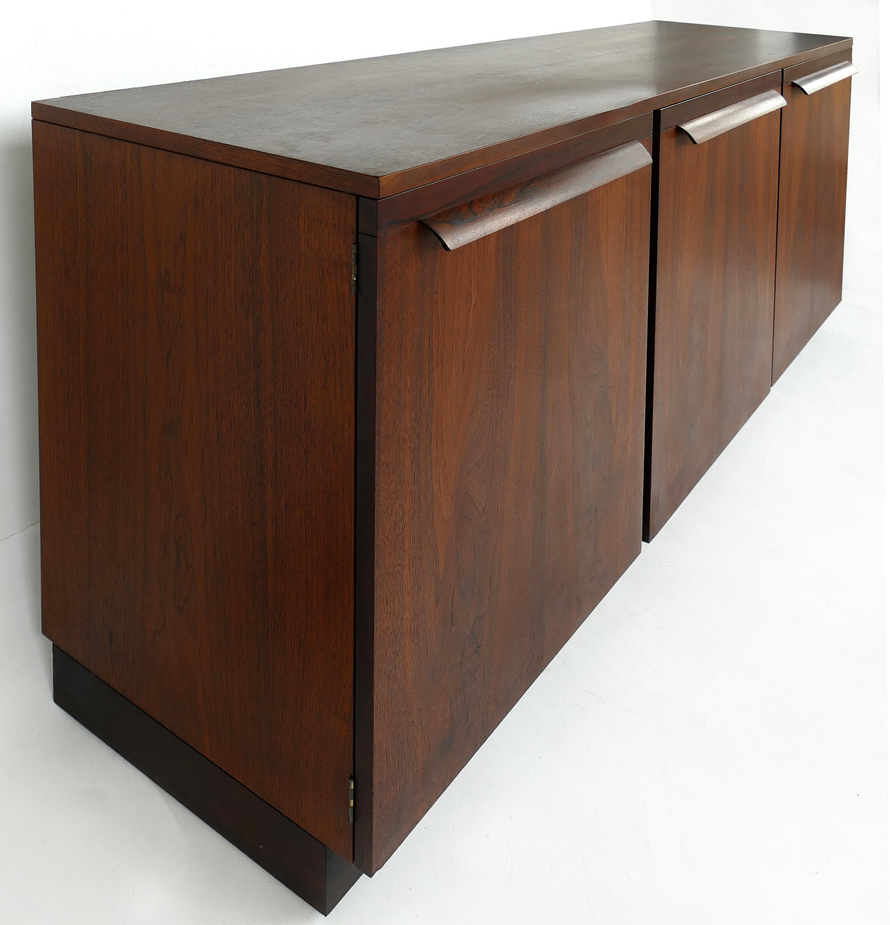 Mid-Century Modern Rosewood Credenza

Offered for is a Mid-Century Modern rosewood credenza with beautifully grained finishes. Two lateral doors open to reveal open shelves. The center door opens to reveal drawers. Each door has a sculptural pull