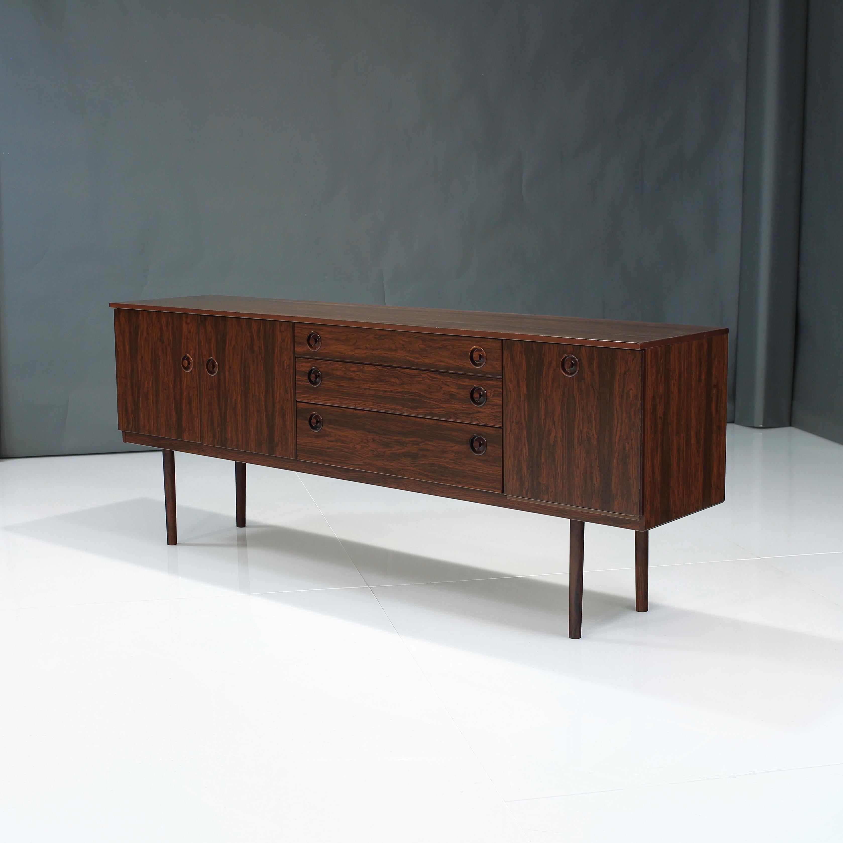 Presenting this long Rosewood credenza from England.

Offering ample storage and stunning visuals with the vivid rosewood grain. 

On the left, you have two cabinet doors with 1 open shelf for storage inside. In the middle you have newly