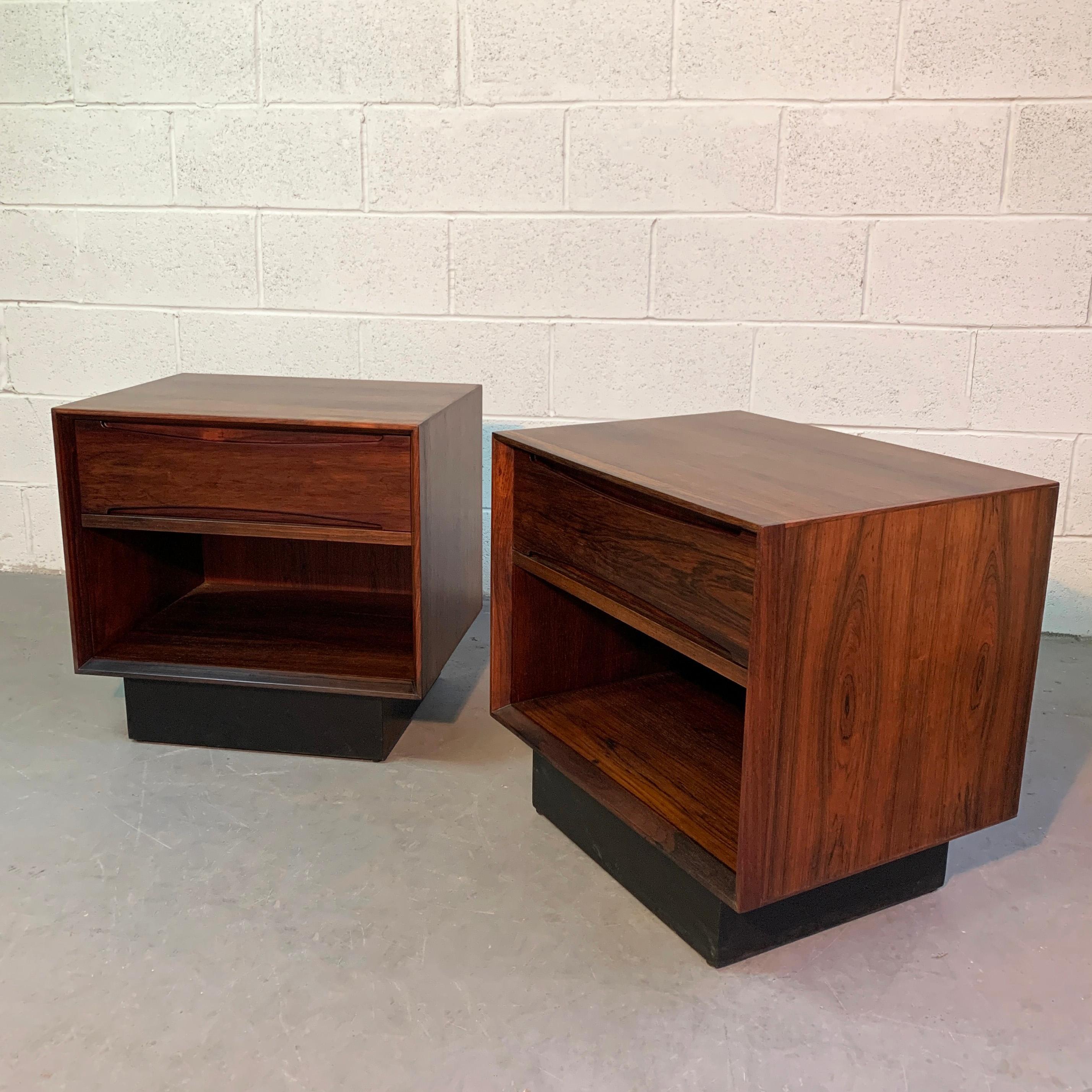 Pair of streamlined, Mid-Century Modern, rosewood cube nightstands or end tables on black lacquered bases feature a top drawer with recessed pulls and open storage below at 8.25 inches ht. They are finished on all sides.