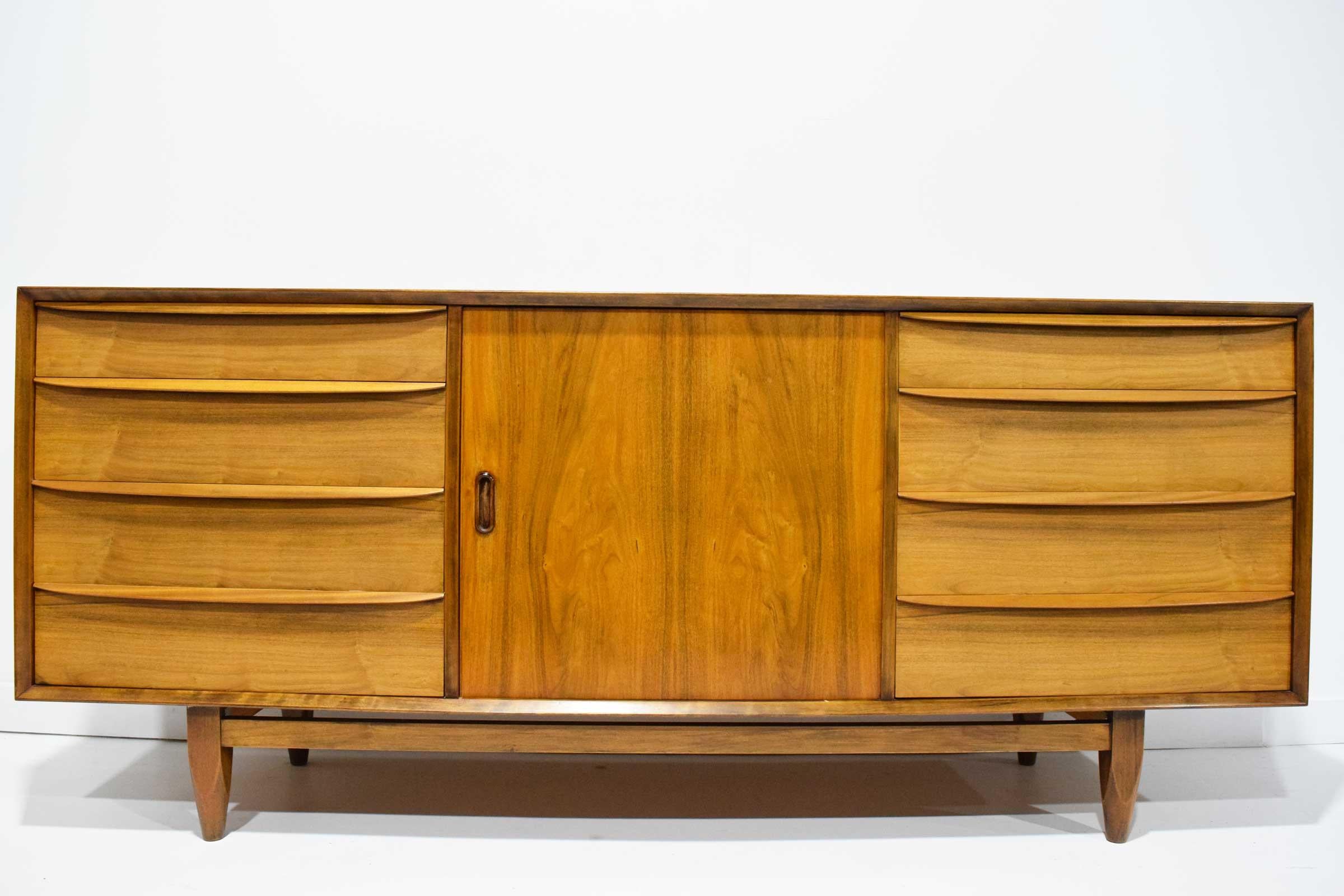 A well made dresser from the midcentury. Finished on back for floating if desired. Front has four drawers on either side with sculptured handles and a door. Behind the door is four additional drawers.