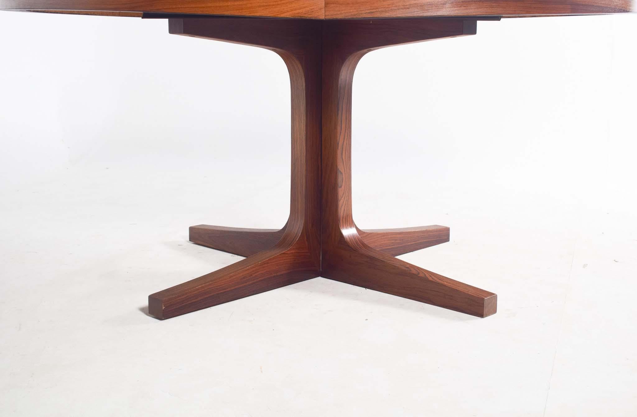 This stunning Mid-Century Modern dining table by Dyrlund, crafted from luxurious rosewood, features an oval top with exquisite grain patterns and two extendable leaves for added versatility. Its sleek design rests on a sturdy pedestal base, ensuring