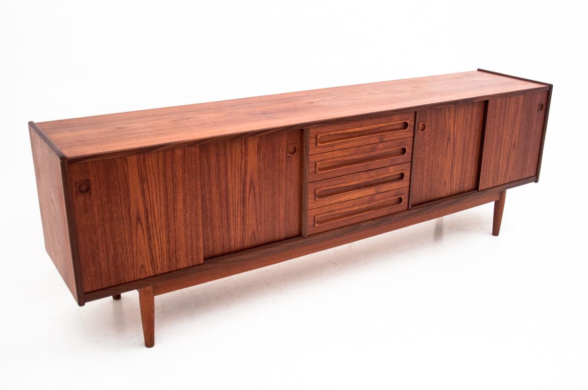 This long vintage sideboard was designed and manufactured in Denmark at the turn of the 1950s and 1960s. In the middle it has 4 spacious drawers lined with green material and sliding cabinets on the sides. Maintained in a very good condition, it