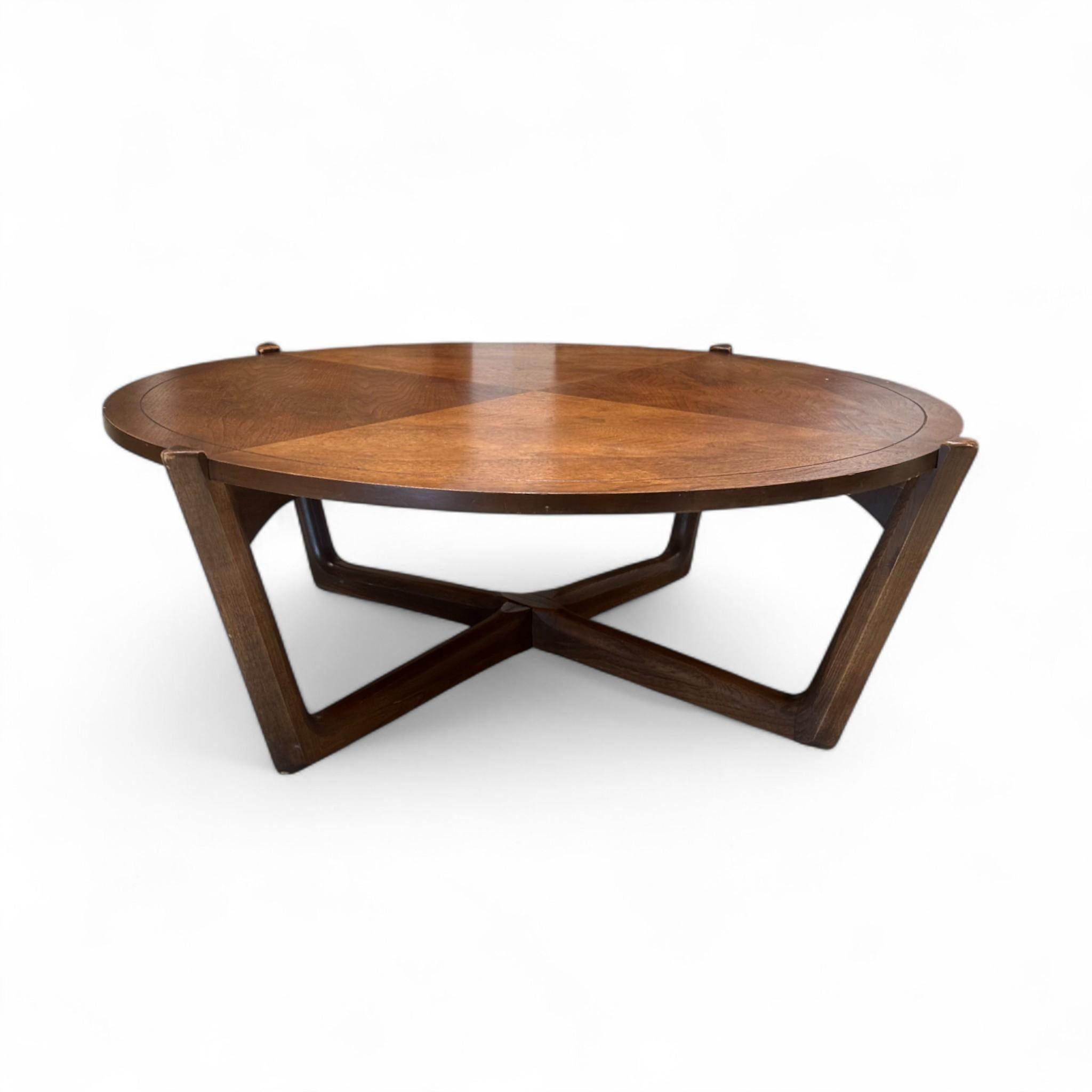 This striking Mid-Century Modern coffee table features a rich walnut finish with a round top showcasing beautiful quadrant wood grain detailing. Its sculptural geometric base adds architectural interest and stability, making it a stylish centerpiece