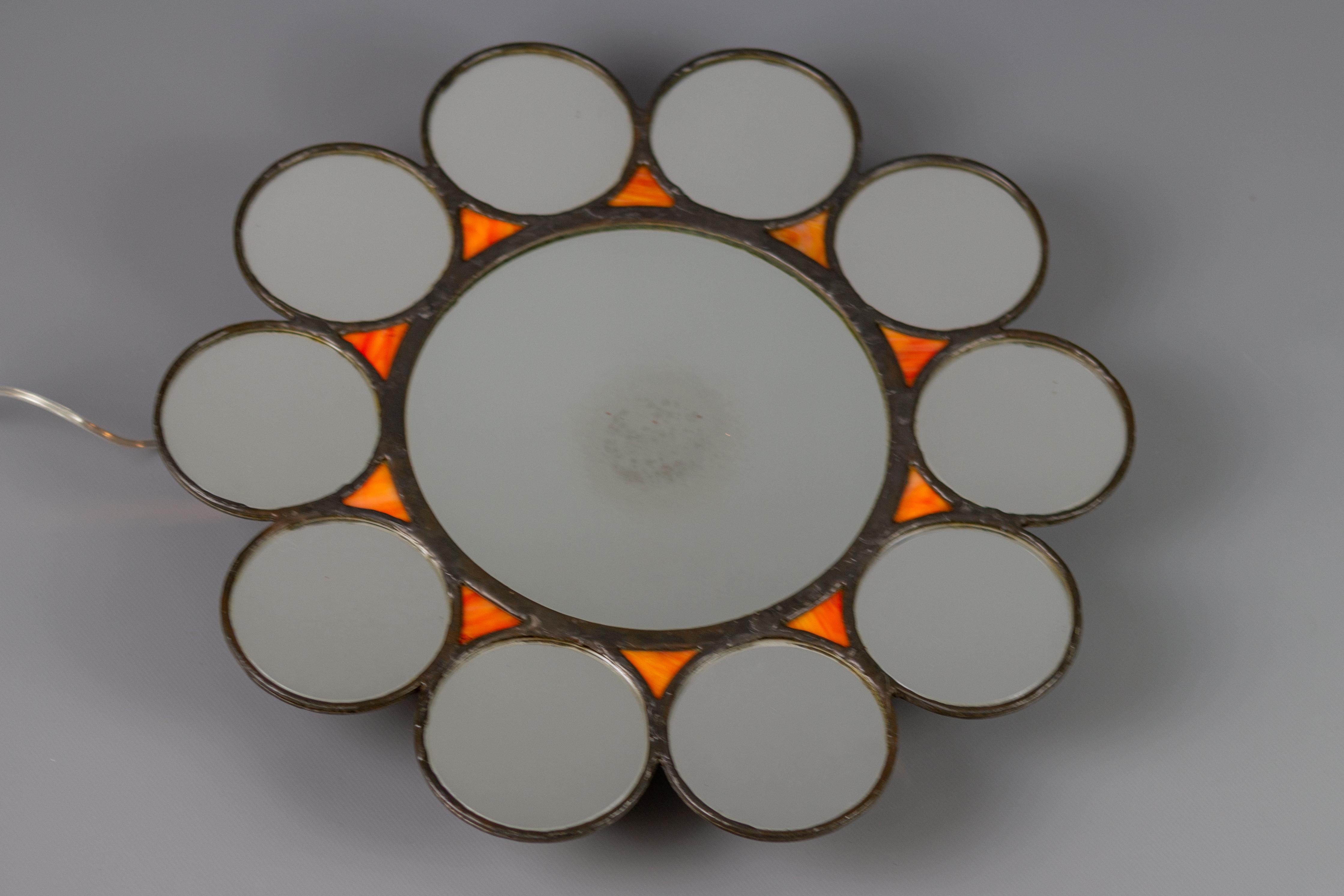 Sun-shaped Mid-Century Modern backlit metal and orange glass wall mirror from the circa 1960s.
Very unusual and rare Mid-Century Modern or Industrial style illuminated backlit wall mirror. This beautiful round wall mirror features a bigger, round