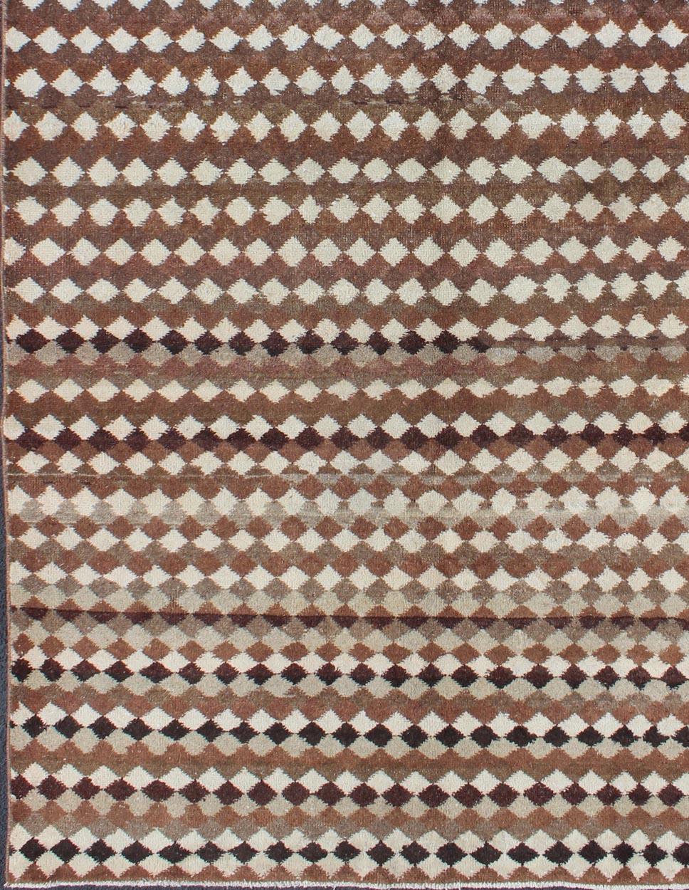 Measures: 5'5 x 9'4.
Set on a brown field with an all-over Modern/Mid-Century Modern pattern, this beautiful vintage rug (circa mid-20th century) features a repeating design of diamond shapes. Accent colors include ivory, cream, charcoal, and