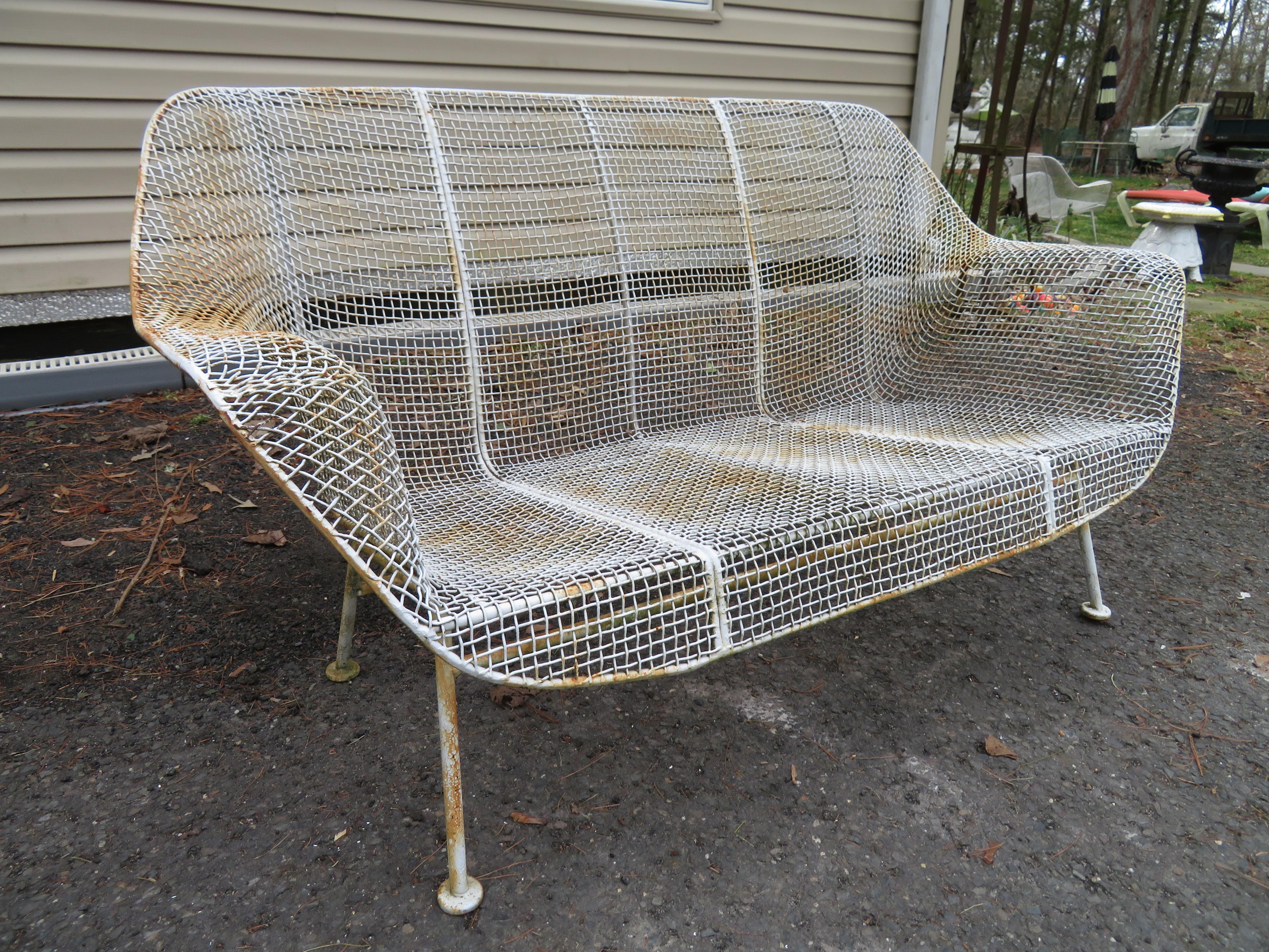 Russell Woodard Patio Sculptura patio bench sofa. It has a wrought iron frame with a low-slung woven mesh steel seat made to withstand all weather conditions. Perfect for outdoor lounging!