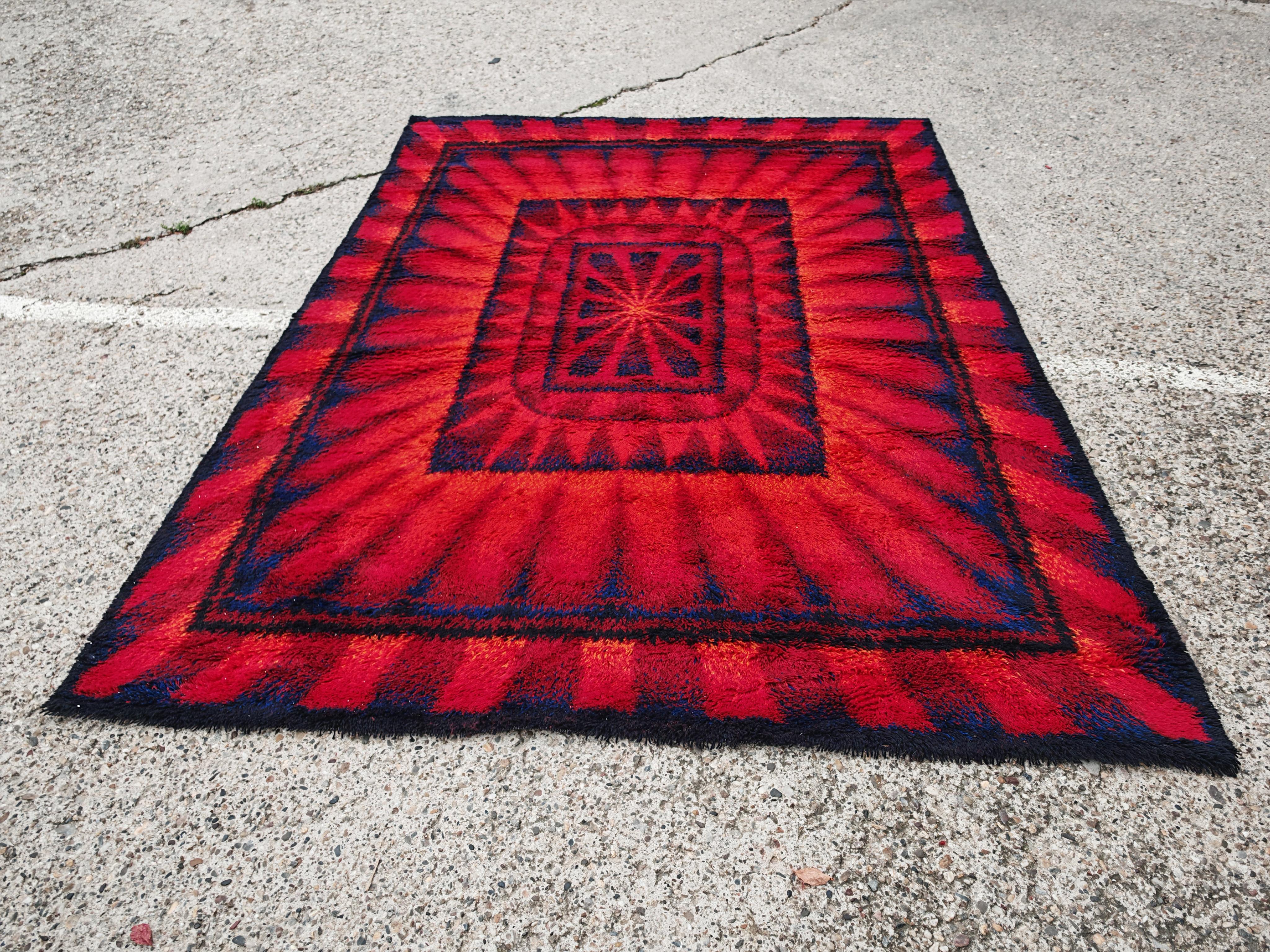 In questa inserzione troverai un tappeto Rya extra large di metà secolo moderno, realizzato nei toni del blu e del rosso e con un bellissimo motivo a forma di sole. Il tappeto è realizzato al 100% in lana e prodotto dall'importante azienda tedesca