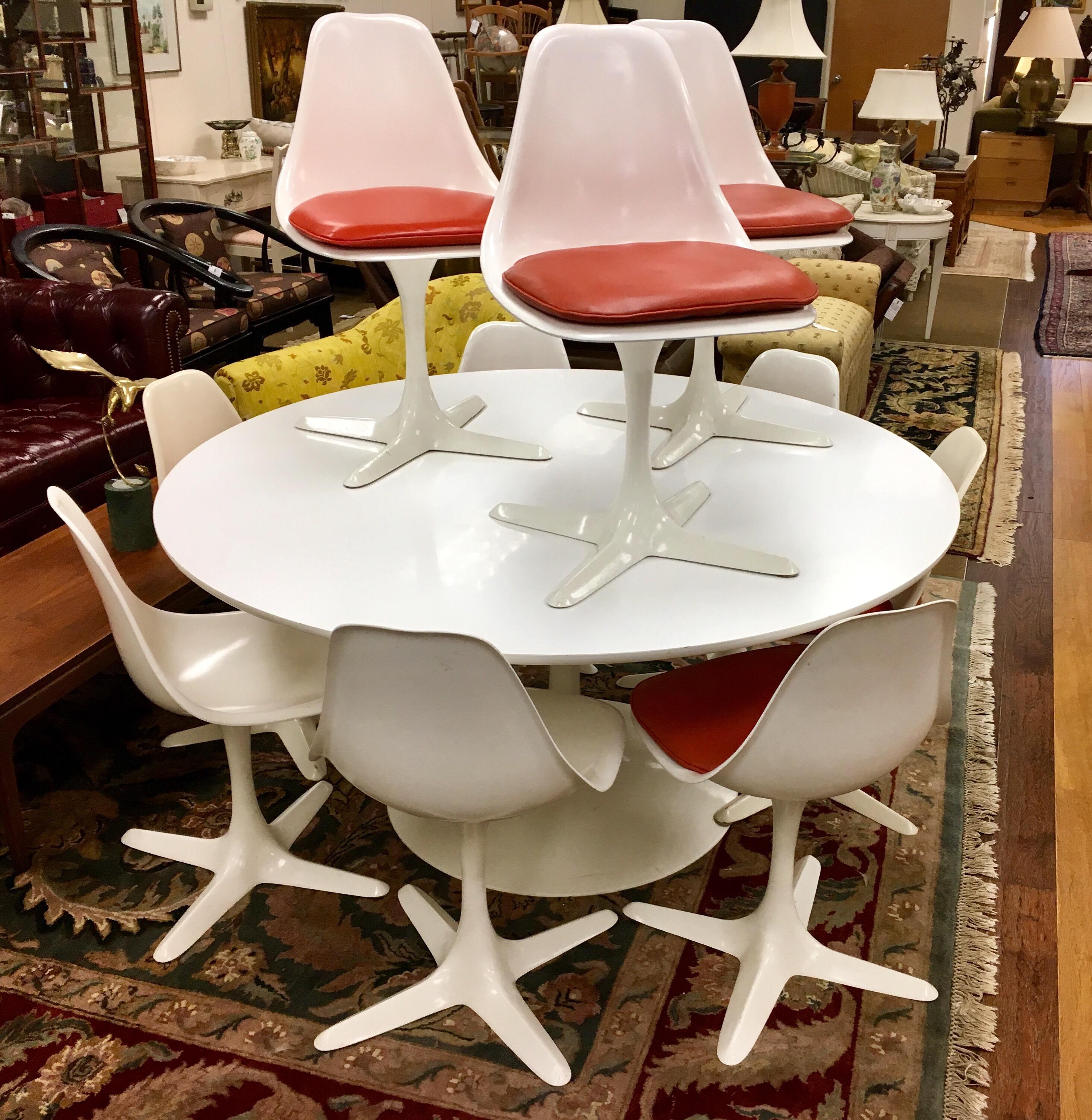 True period tulip set from famed vintage USA maker Burke Industries that features a five foot round tulip table and ten matching chairs. Eight of the ten chairs have a custom reddish orange seat cushions, the other two do not.