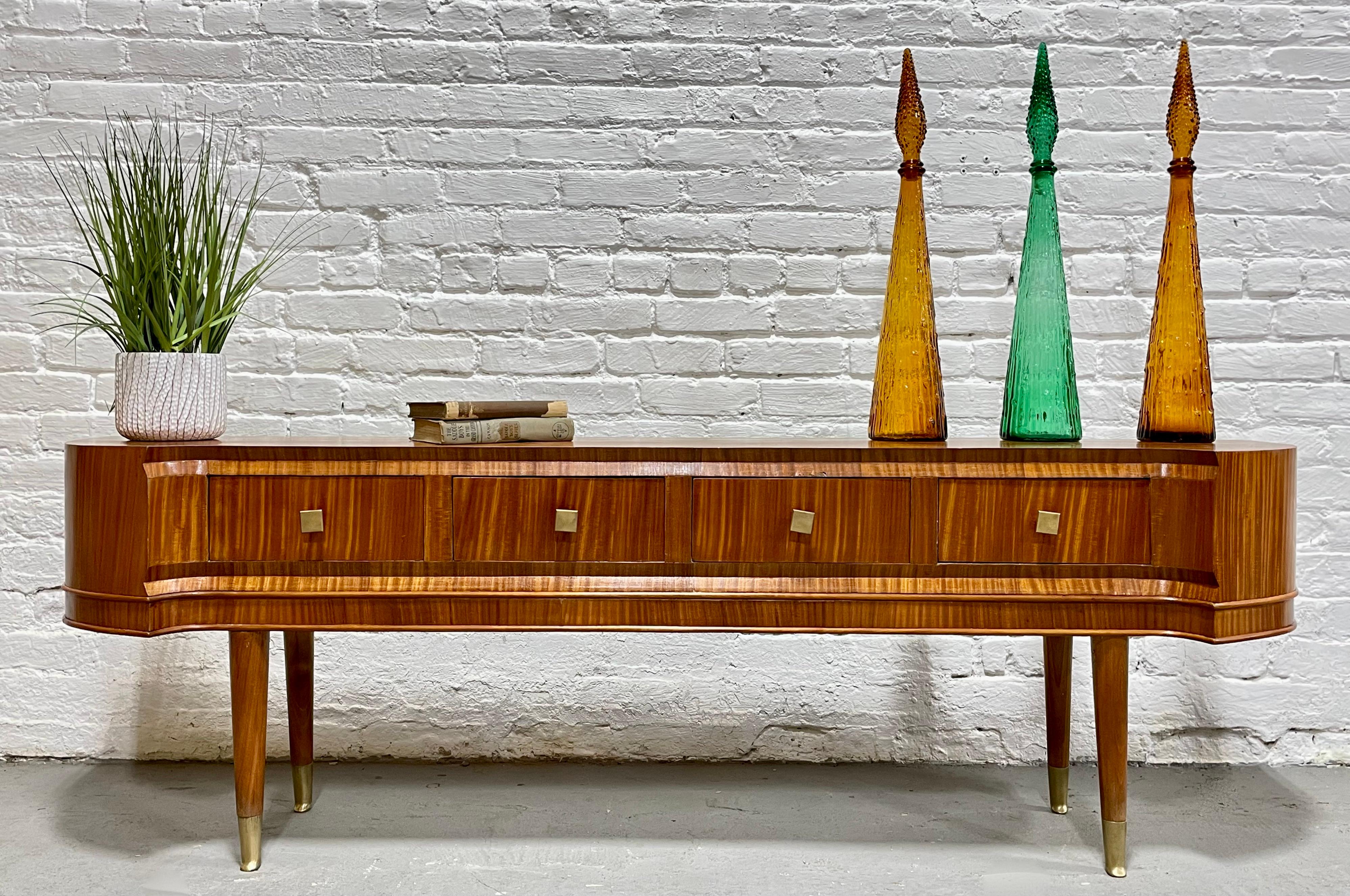 One of a kind French Mid Century Modern Sapele Wood Console Table, c. 1950's. This superbly crafted piece offers outstanding vibrant woodgrain, long tapered brass capped legs and four drawers with square brass pulls. The console offers a fairly low