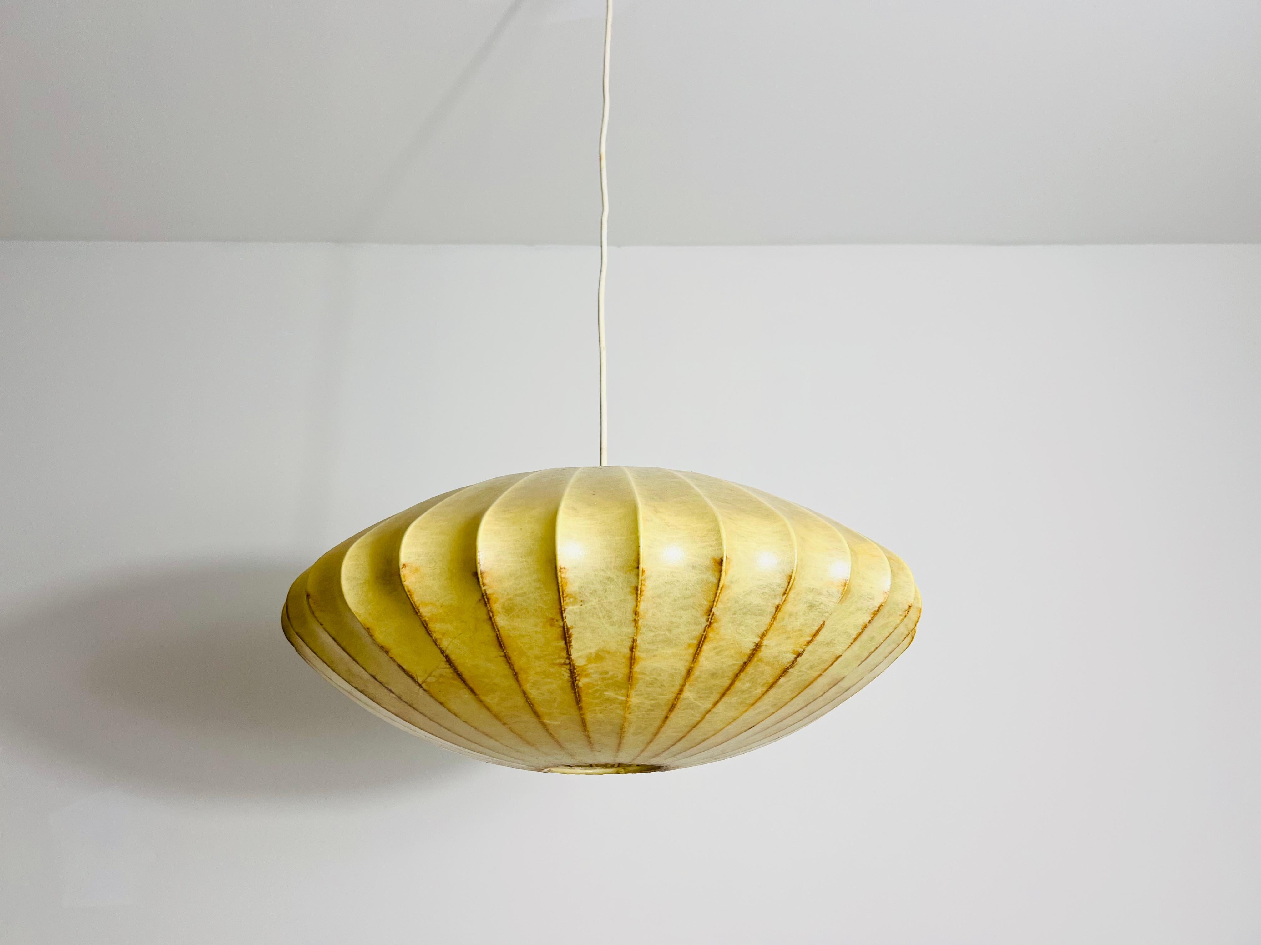 Questa lampada da soffitto a forma di piattino a bozzolo degli anni '60 emana un'eleganza senza tempo e un fascino vintage. Il materiale del bozzolo, caratteristico del design moderno di metà secolo, ha sviluppato una bella patina nel corso degli