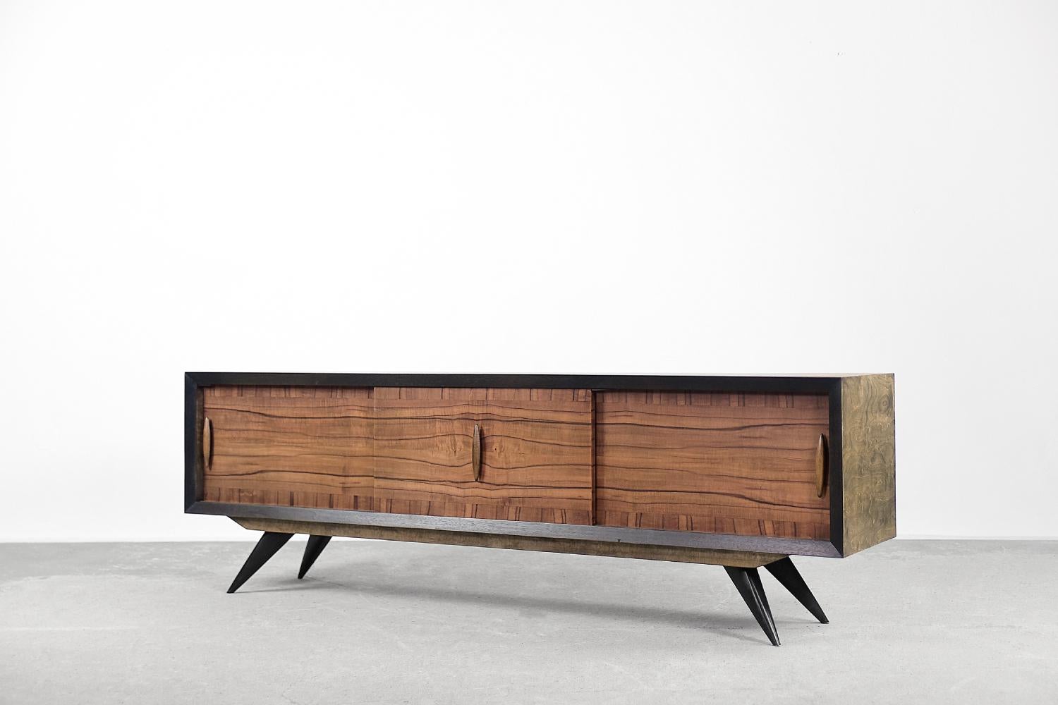This modernist sideboard comes from Scandinavia, where it was created during the 1960s. The top and sides are finished with birch wood with a strong, irregular grain. The front is made of walnut wood in natural tone. The sideboard has three sliding