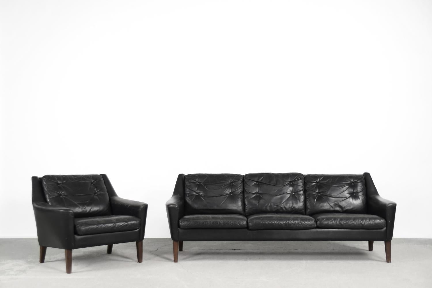 This lounge set consists of a three-seater sofa and an armchair, was manufactured by the Swedish Ulferts Tibro during the 1960s. This set is finished in black natural leather and has loosely placed cushions. The frame is characteristically up and