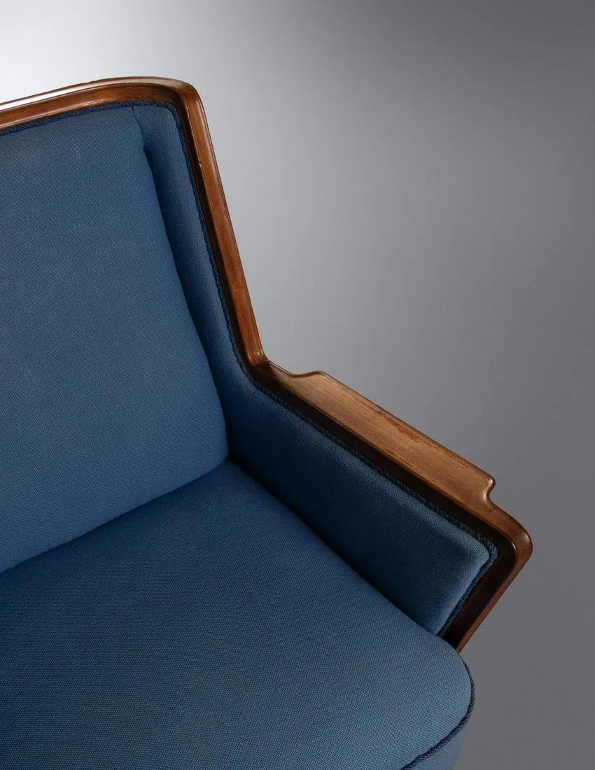 A timeless Mid-Century Modern finish cabinetmaker lounge chair with a finely hand carved mahogany frame featuring a pointy armrest and a rail wood molding design while standing out in a dark blue original upholstery. Stylish and comfortable, the