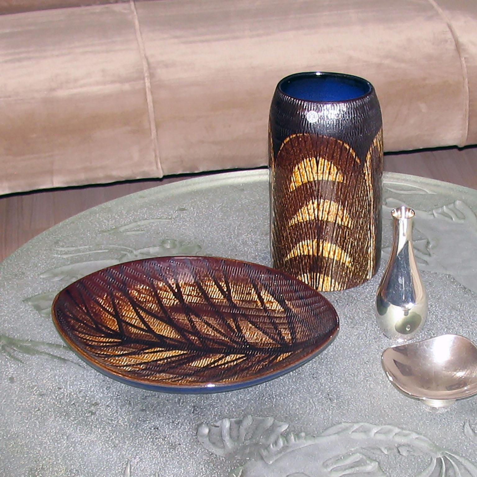 Mid-Century Modern Scandinavian ceramic vase and tray.
Amazing pottery of the 1960s by Ingrid Atterberg for Upsala Ekeby, depicting a textured leaf motif with brown and yellow contrast, inside of the vase and backside of tray in dark royal blue.