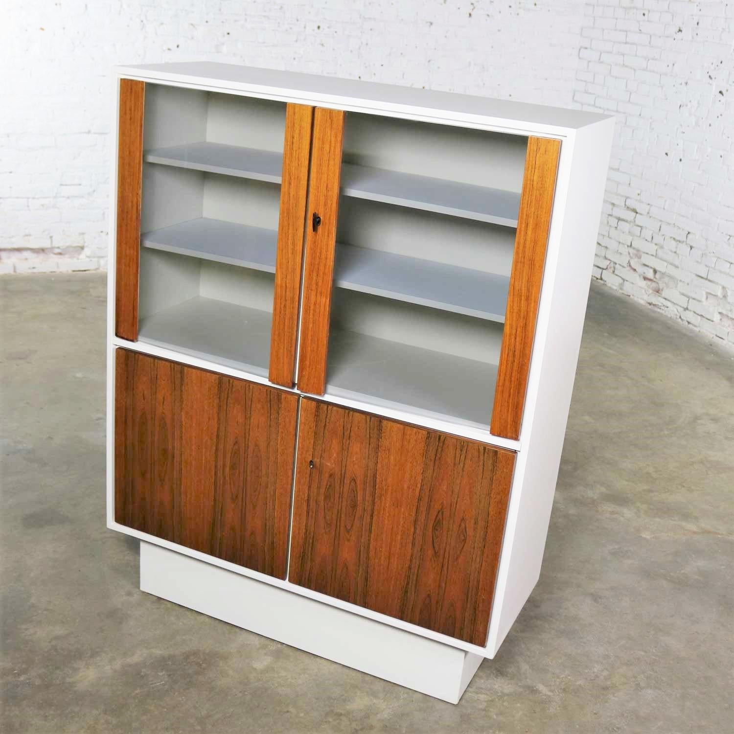 Toller Geschirr- oder Vitrinenschrank im Mid-Century Modern- und/oder Scandinavian Modern-Stil mit einem cremeweiß lackierten Gehäuse auf einem Sockel und Türen aus Teakholz und Glas. Dieses Stück ist in fabelhaftem Zustand. Die weiße Lackierung