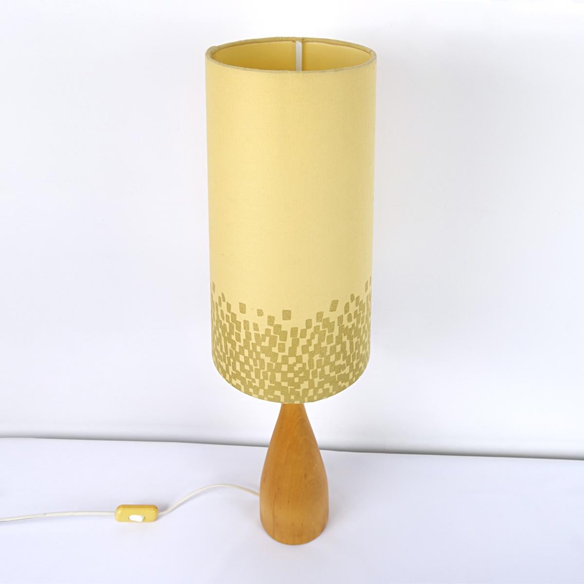 This elegantly shaped lamp foot has a slim waist and carries a soft yellow conic shade of which the bottom part is set with square gold colored cubes in a random pattern. 
The lamp is marked underneath the foot: Nr. 041. There is also a stamp which