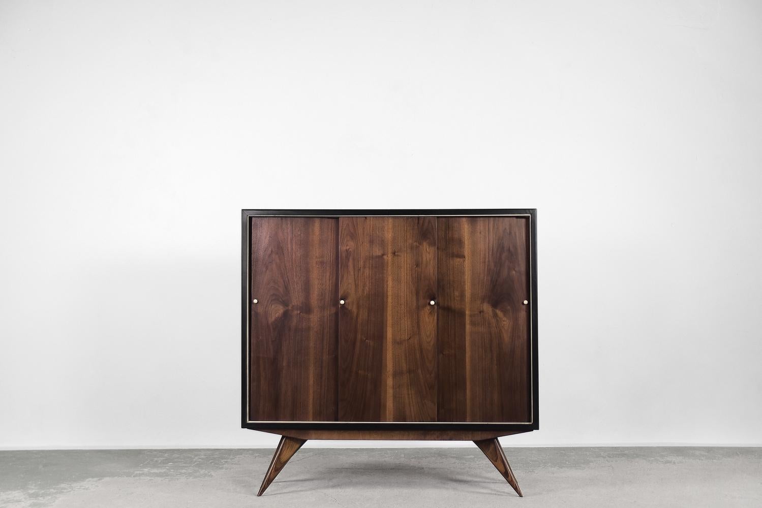 This classic cabinet was made in Scandinavia during the 1960s. This piece was finished with high-quality walnut wood with a dark, noble color and distinctive graining. It has three sliding doors. The black and white round handles give the object a