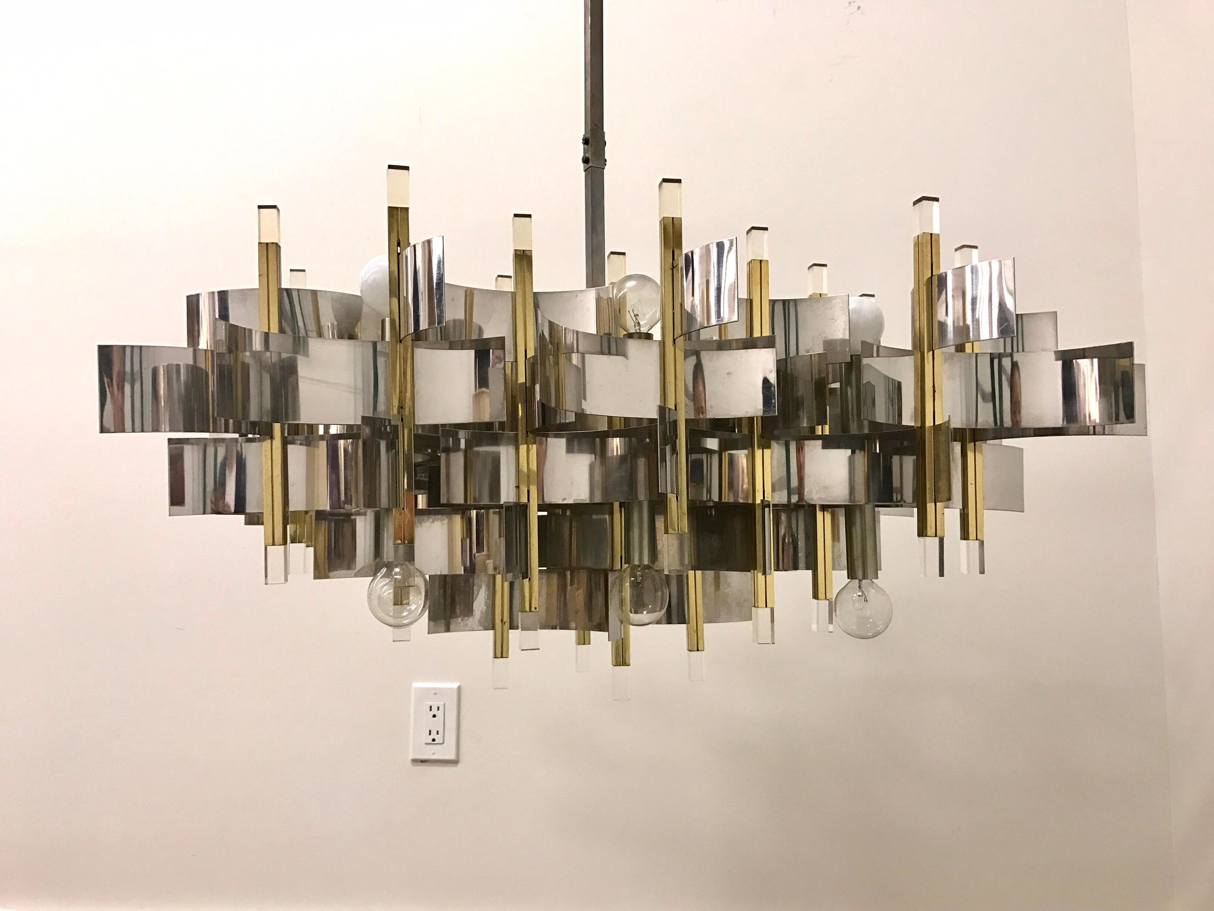 This truly exceptional and iconic chandelier was realized by the esteemed Italian midcentury lighting atelier, Sciolari, circa 1970. It features a wealth of curvilinear nickel bands that connect to polished brass rectangular rods capped with Lucite