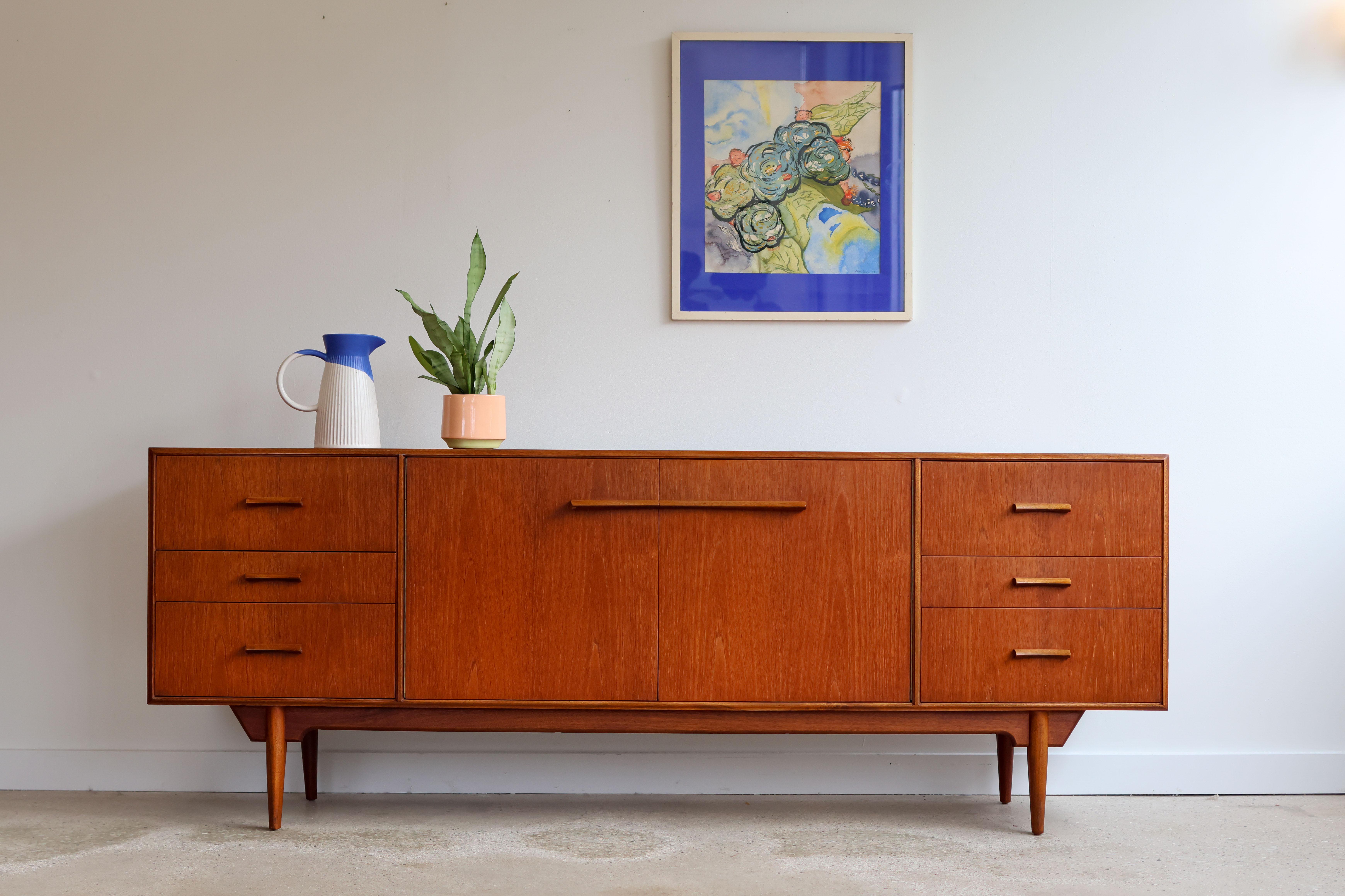 Mid-Century Modern teakwood sideboard.
Unique design by McIntosh, Scotland, 1960s.
Six dovetailed drawers with oak handles.
Double cabinet doors with stationary shelving inside.
Beautifully refinished top.
Excellent vintage condition.

79 1/4” long