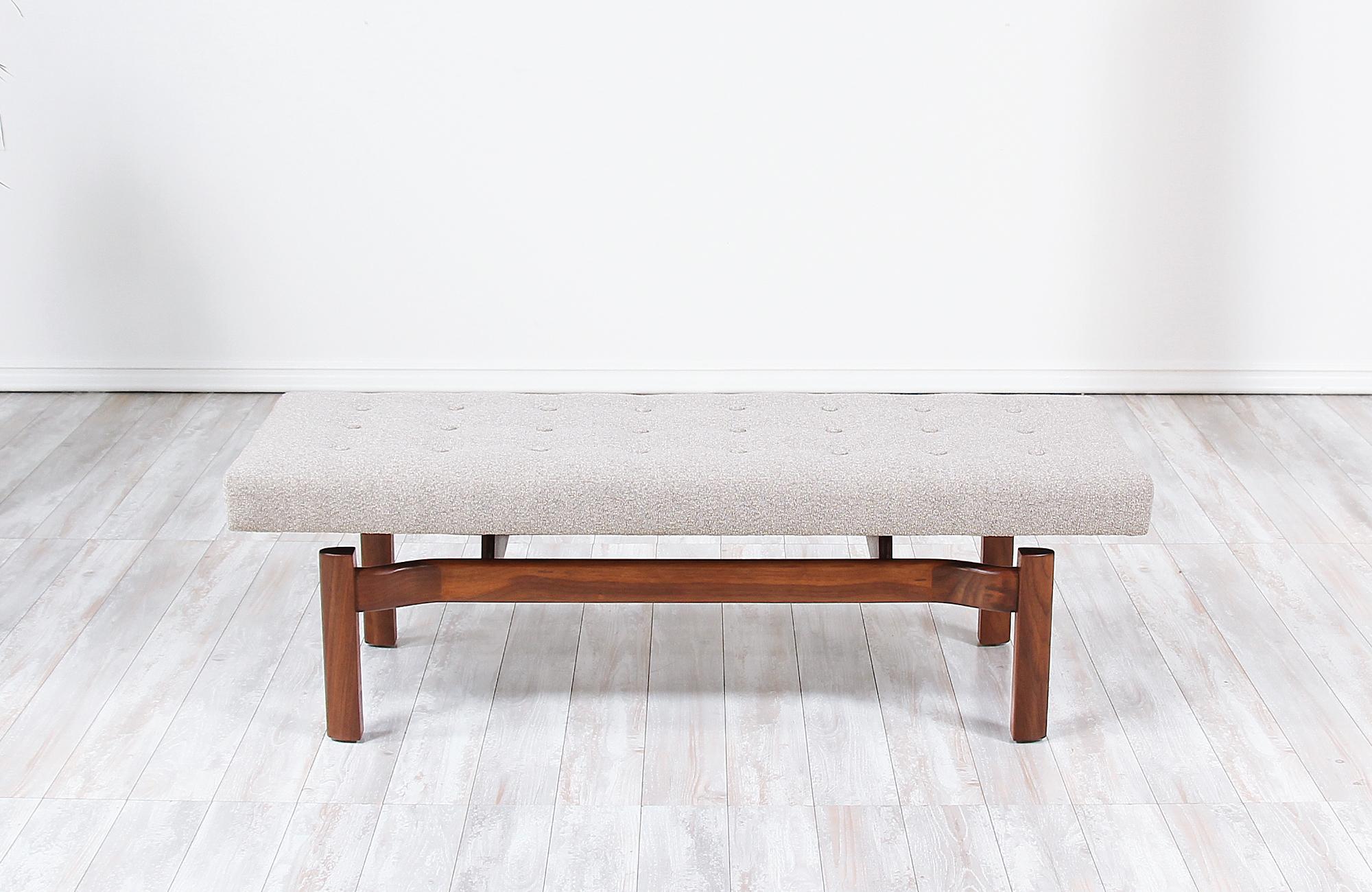 Mid-Century Modern bench designed and manufactured in the United States, circa 1950s. This elegant bench features a solid walnut wood frame with a newly upholstered cushion that seems to float over the base creating a look of sophistication. The