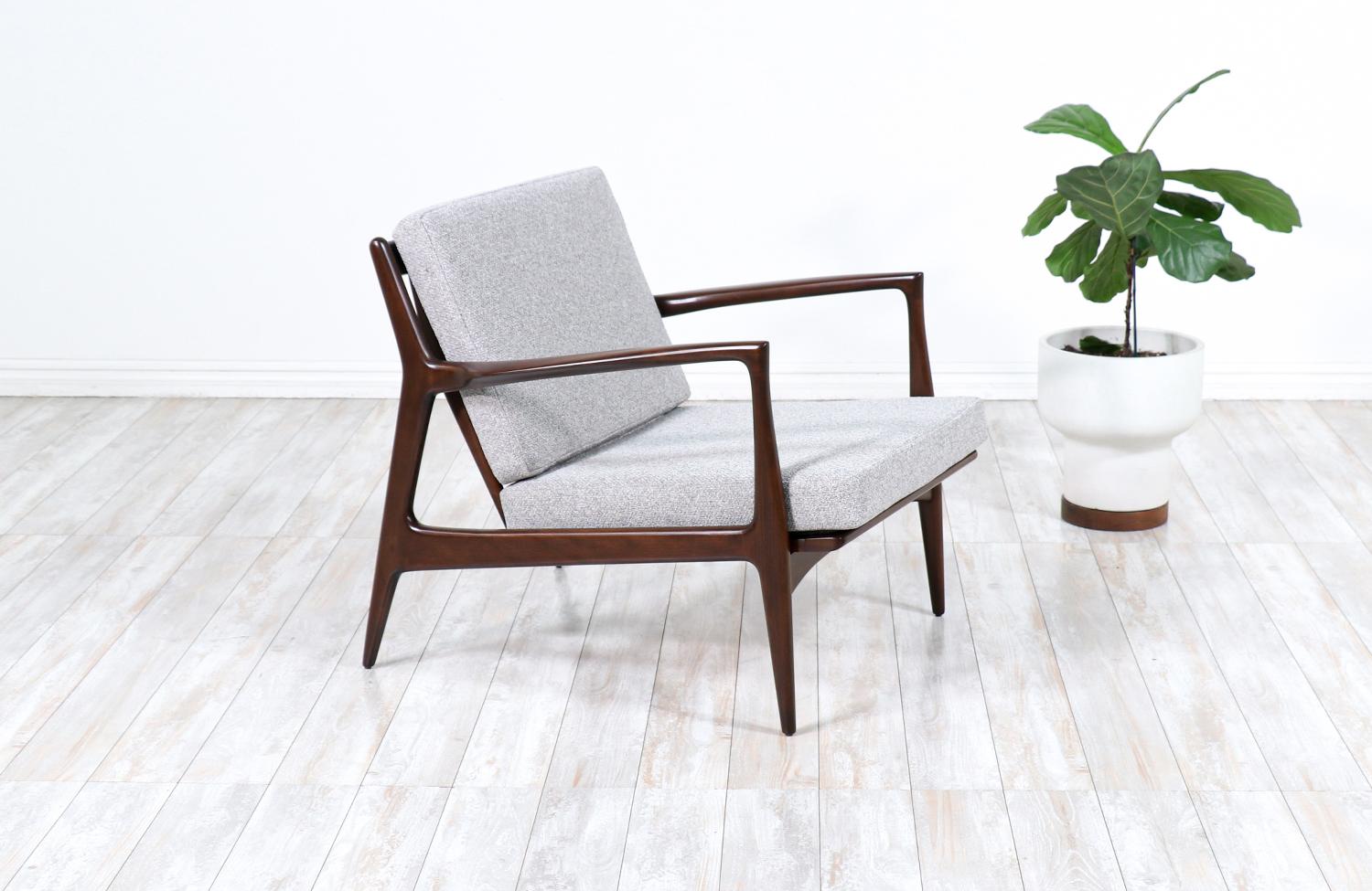 Stylish lounge chair designed by Ib Kofod-Larsen for Selig in Denmark circa 1960s. This sleek and ergonomic lounge chair features a sturdy walnut-stained beechwood frame with angled legs and a sculptural slatted back that is held in place by a bowed