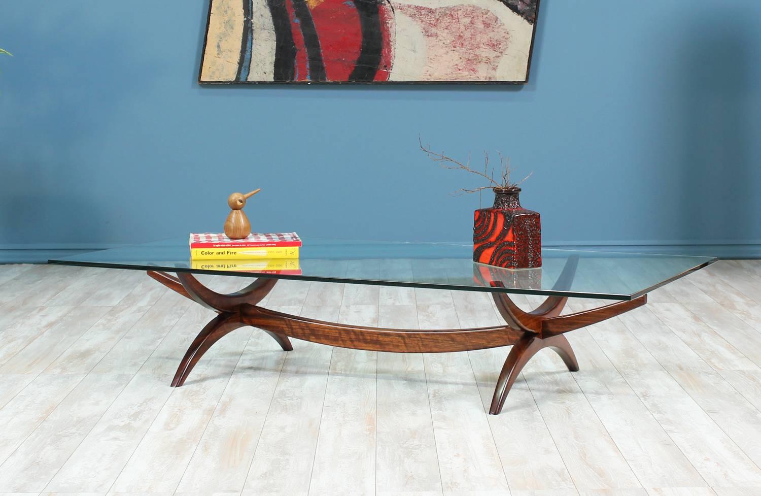 Elegant Mid-Century Modern rosewood coffee table designed and manufactured in the United States circa 1960’s. This stunning coffee table features a new glass top. The transparent glass top permits you to appreciate the beautifully sculpted,