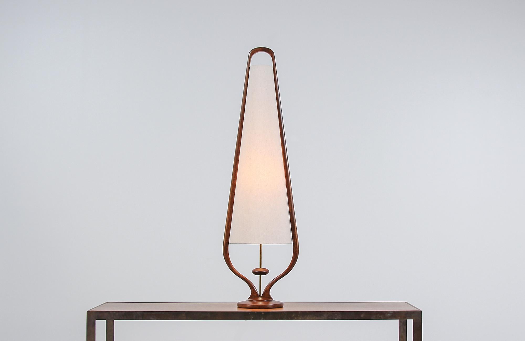 Modern table lamp designed and manufactured by Modeline of California in the United States circa 1960s. This tall table lamp features a rounded walnut wood base with a sculpted frame that embraces the new linen shade and accentuates the newly