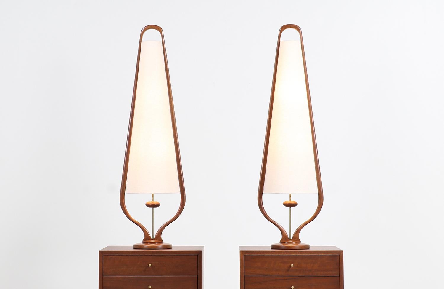 A stylish pair of modern table lamps designed and manufactured by Modeline of California in the United States, circa 1960s. These tall table lamps feature a rounded walnut wood base with a sculpted frame that embraces the new linen shade and
