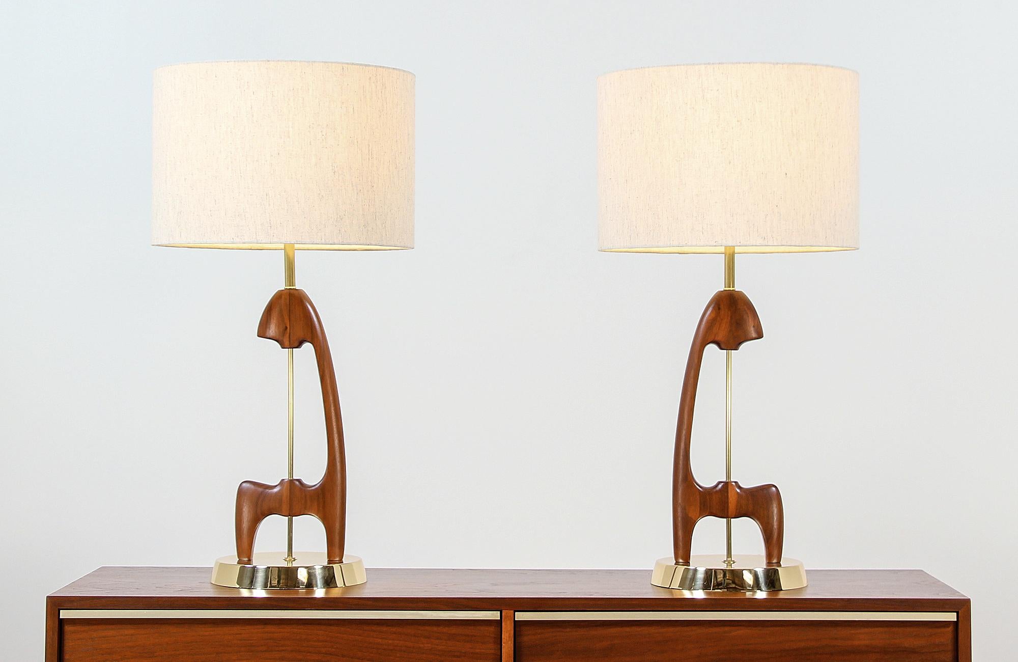 Dazzling pair of modern table lamps designed and manufactured in the United States circa 1960s. This stunning Mid-Century Modern lighting design features a sculptural walnut body with newly polished brass base and hardware complemented with varying
