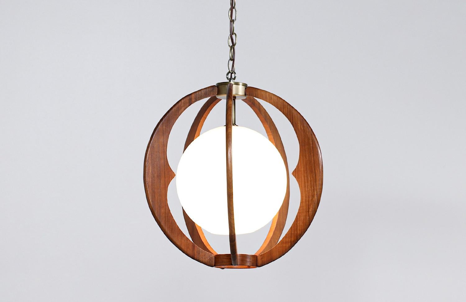 Modern globe pendant chandelier designed and manufactured in the United States circa 1960’s. This delicate chandelier features a white glass shade enclosed in a spherical walnut wood frame with brass accents. This beautiful design is subtle yet