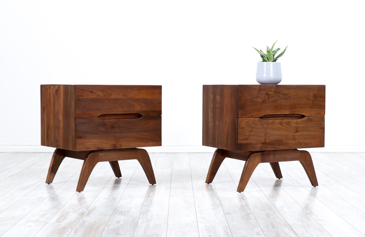 Pair of Mid Century Modern night-stands designed and manufactured in the United States circa 1960’s. These elegant night-stands feature a walnut wood case with two dovetailed drawers with recessed pulls. The boxy case sits on a sculpted base with