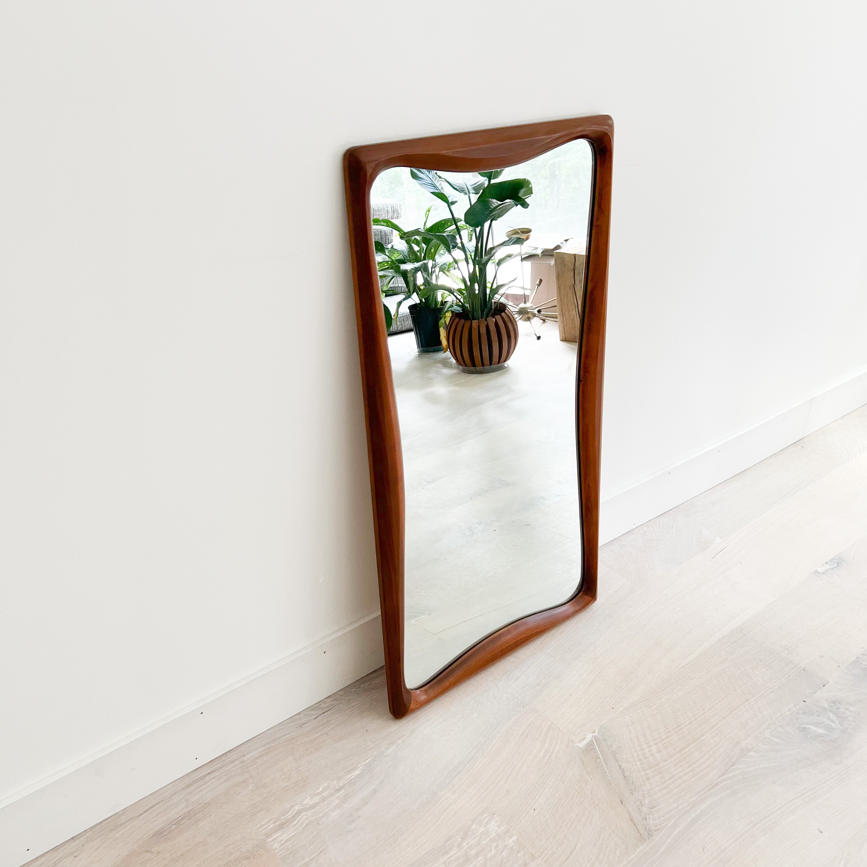Unique Mid-Century Modern mirror with sculpted walnut sides by Bassett Furniture. Some light scuffing/scratching to the wooden frame and mirror from age appropriate wear.
 