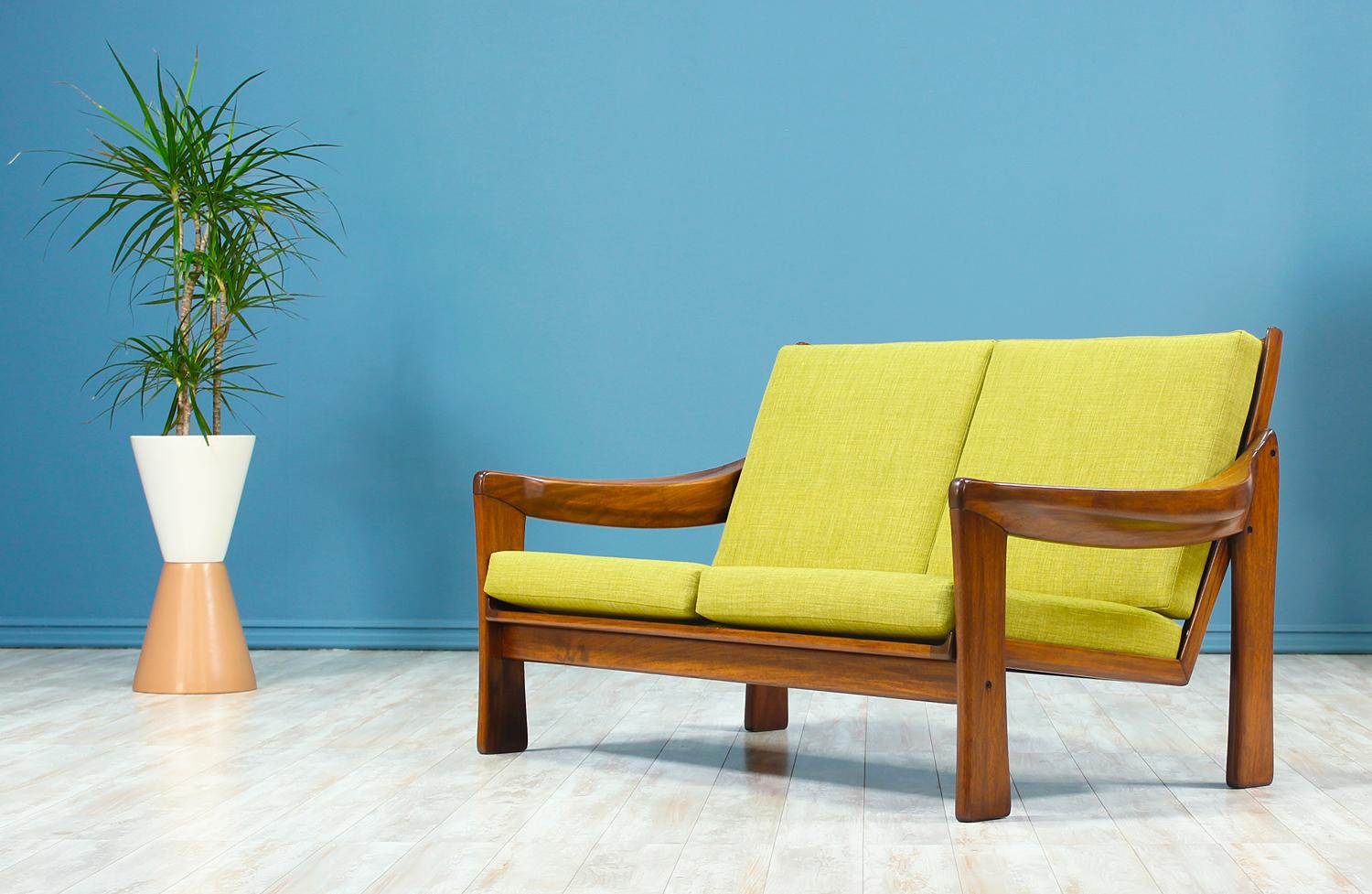 Wonderfully sculpted wood settee manufactured in the United States, circa 1960s. This Mid-Century Modern settee is crafted in solid mahogany wood and features new high-density foam loose cushions recently upholstered in a quality green fabric. The
