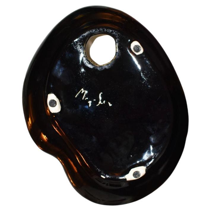 A sculptural Mid-Century Modern ceramic ashtray. This piece is in cream, and in an unusual oblong shape. The bottom is glazed in black, with a small illegible signature. The top is handpainted and glazed in a brown foliage bamboo design. Use this