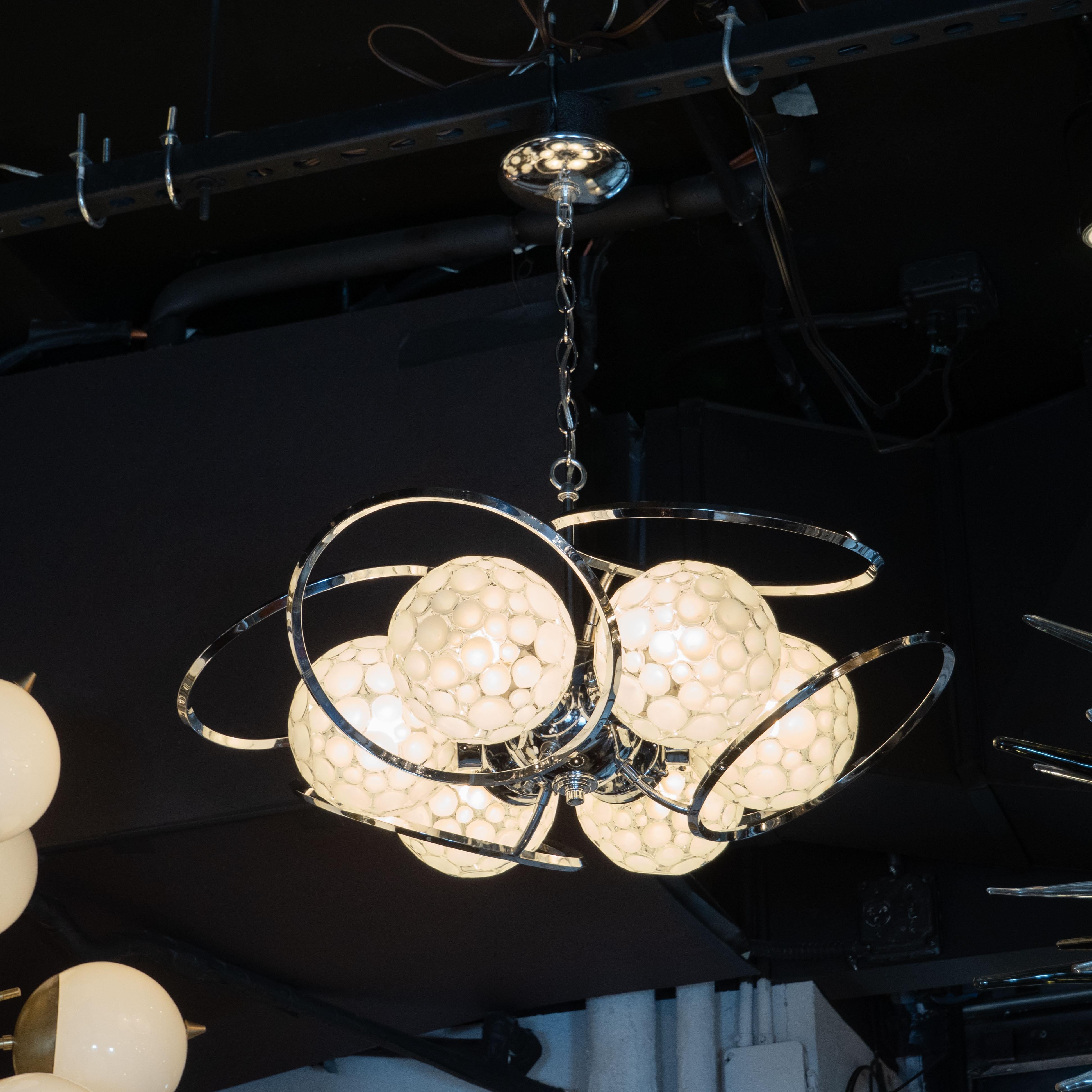 This graphic and sculptural Mid-Century Modern chandelier was realized in the United States circa 1960. It offers six orbital globes adorned with an abundance of concave white glass embellishments surrounded by curvilinear chrome forms resembling