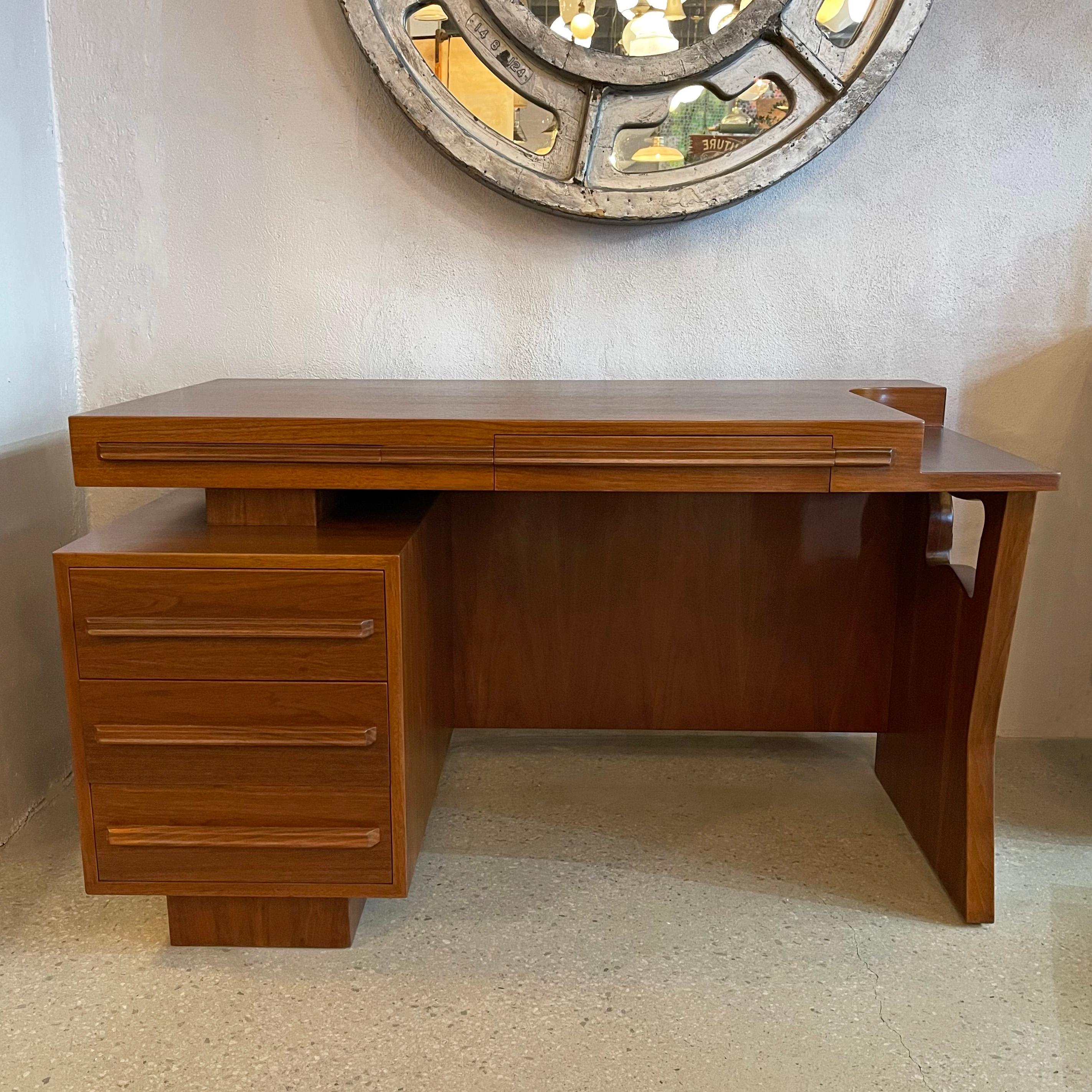 Mid-century modern, walnut desk has numerous outstanding features. The split-level floating top has a curved indentation, concealed segmented drawer and pull-out ledge for additional work surface. There is a decorative, biomorphic cut-out on one