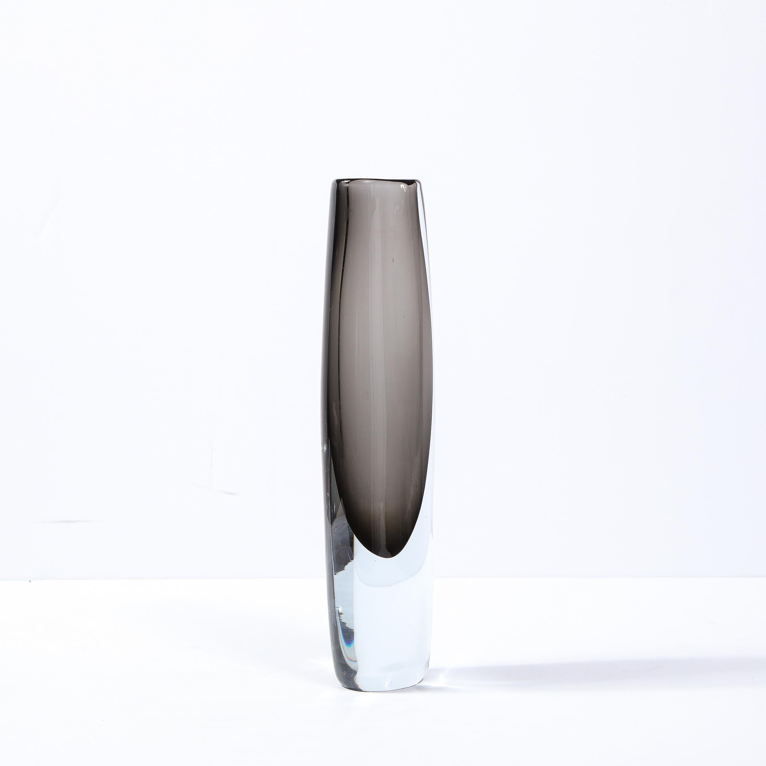 This stunning Mid-Century Modern vase was realized by the esteemed maker Holmegaard in Sweden circa 1960. It features a dynamic, subtly asymmetrical cylindrical body with an amorphic teardrop center in sultry smoked gray glass surrounded by
