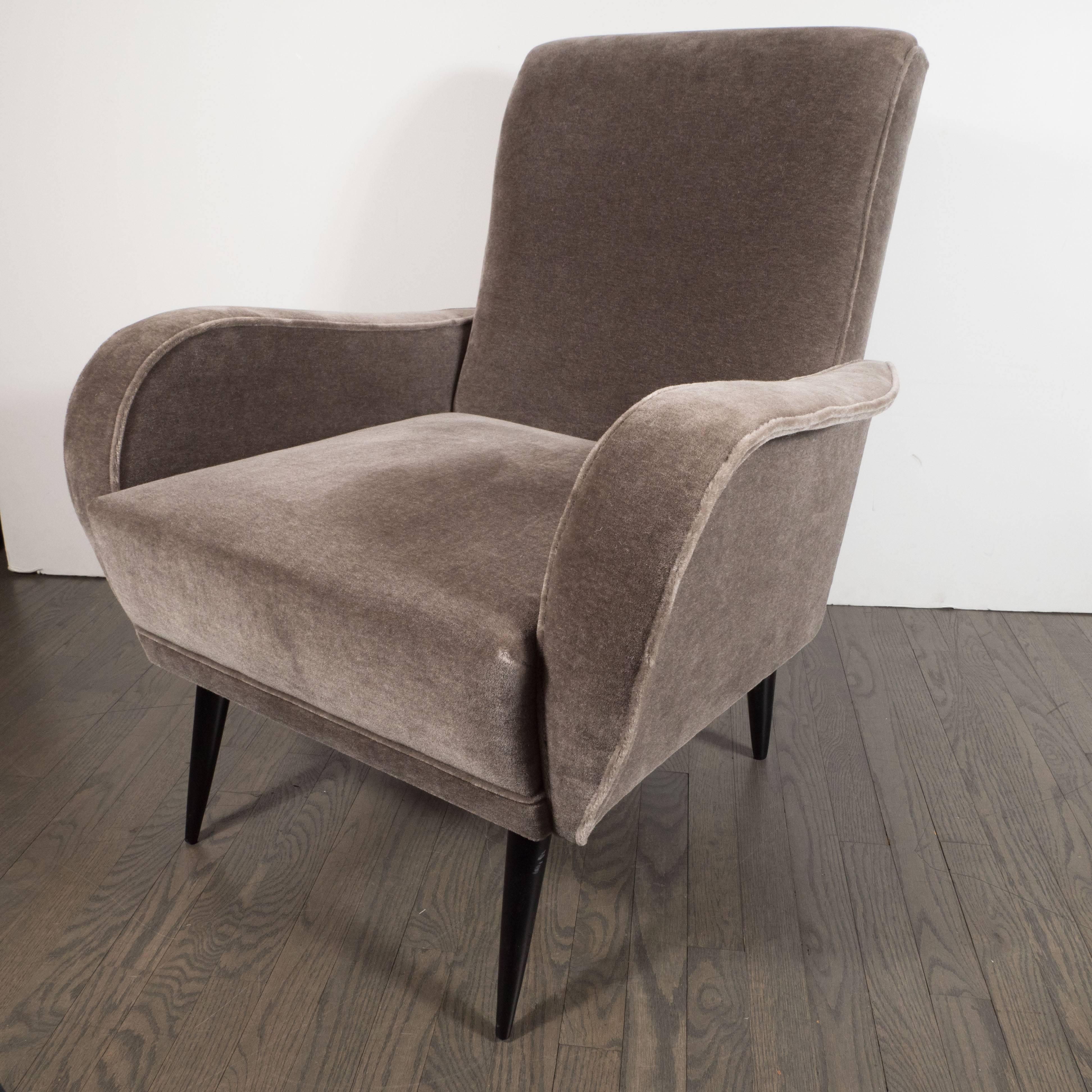These elegant lounge chairs were realized in Italy, circa 1950. Realized in the manner of Marco Zanuso, they feature gently tapered backs; conical ebonized walnut legs; and streamlined arms whose outer edge dramatically flares out, resembling