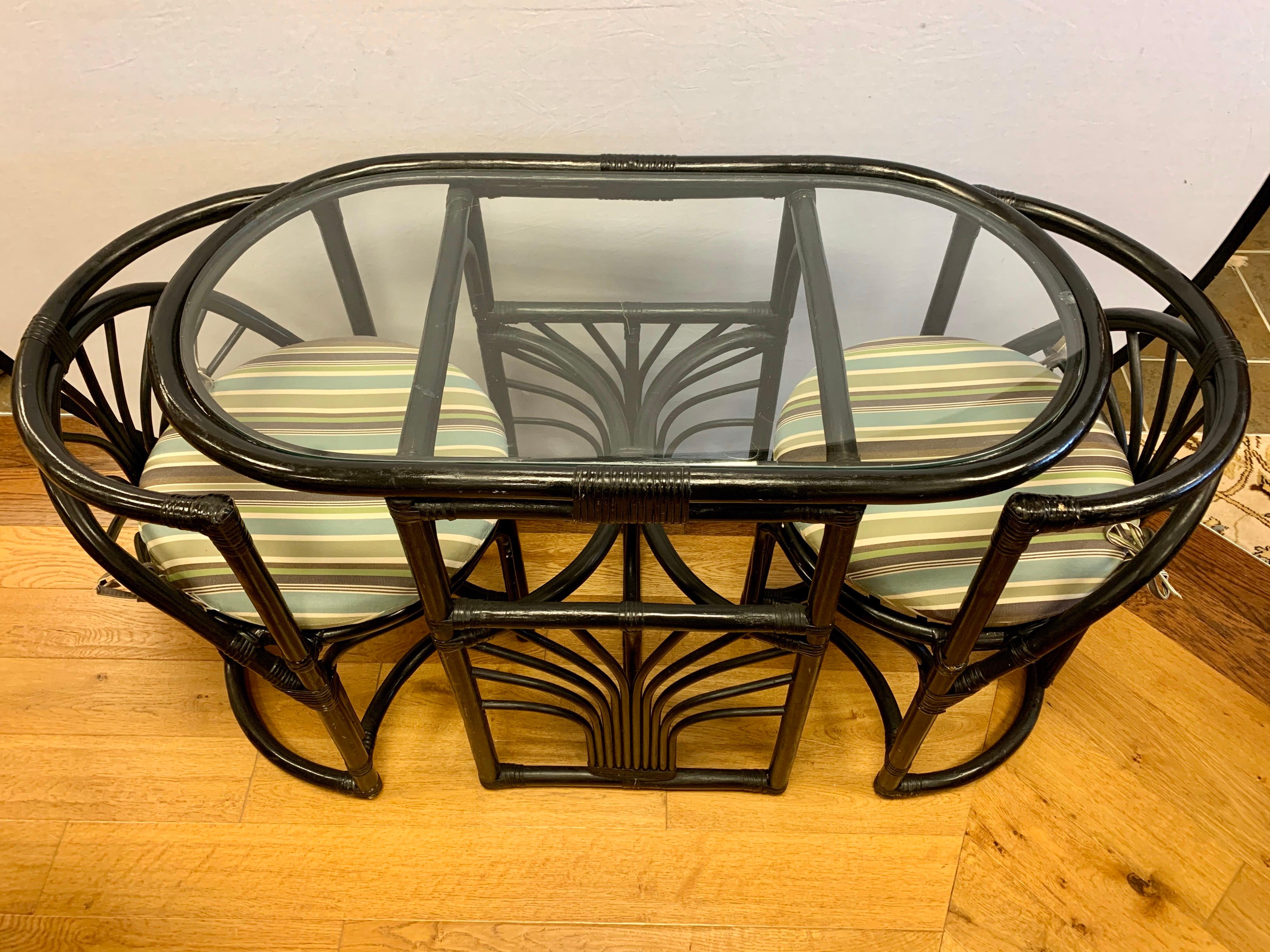 Rare three piece Paul Frankl style oval bistro set. Includes an oval rattan/bamboo table with glass top and two curved chairs that nest inside and then pull out. There is a separate seat cushion on each chair. The set was hand painted black back in
