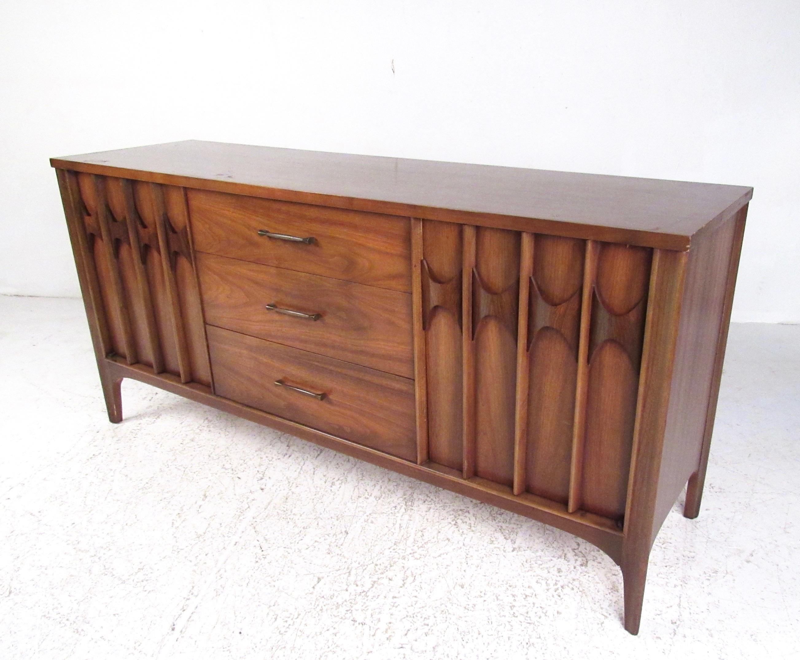 This unique Mid-Century Modern sideboard features walnut finish and a spacious mix of drawers and cabinets for efficient storage at home or office. Brasilia style sculptural door fronts add a unique modernist flair to this elegant storage credenza.