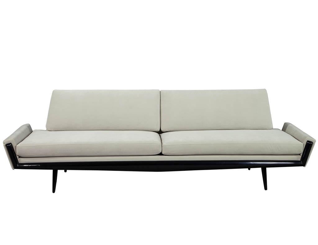 Stunning example of midcentury design. This unique midcentury sofa features a stylish walnut frame hand polished in an ebonized finish. With Classic tapered and sculpted armrests and seat back, sporting loose cushions. Recently reupholstered in a