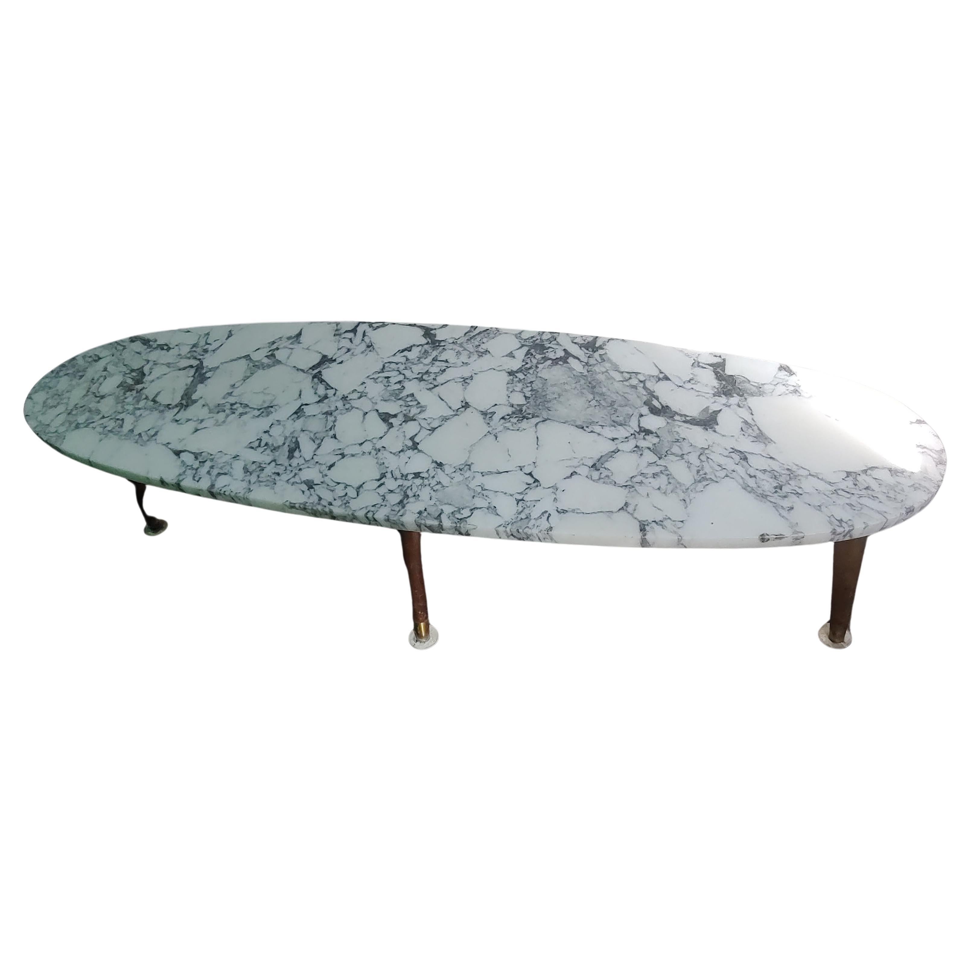 Fabulous simple yet elegant surfboard shaped cocktail table in carrara Marble. Four walnut legs with brass sabots for support. Marble sits on a plywood base. In excellent vintage condition with no chips or damage. Very well taken care of.