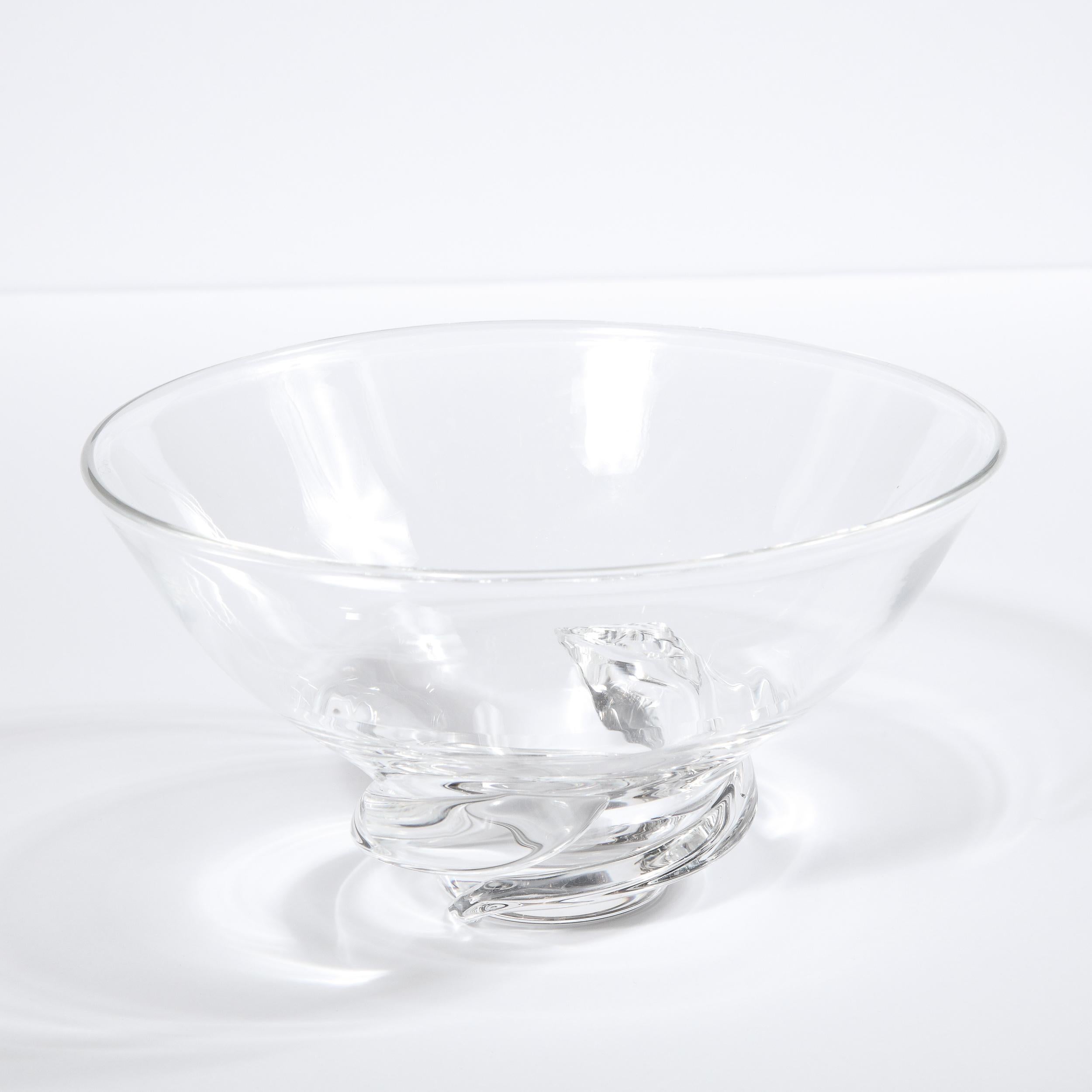 This refined Mid-Century Modern bowl was realized in the United States by the esteemed maker Steuben circa 1960. It features a sculptural swirling base and a subtly flared circular mouth in translucent glass. While this is a perfectly functional