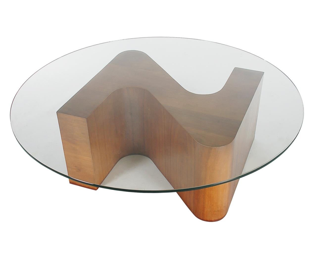A 48 inch circular cocktail table from the 1960s. It features a sculptural form base in American walnut, with a thick round clear glass top.