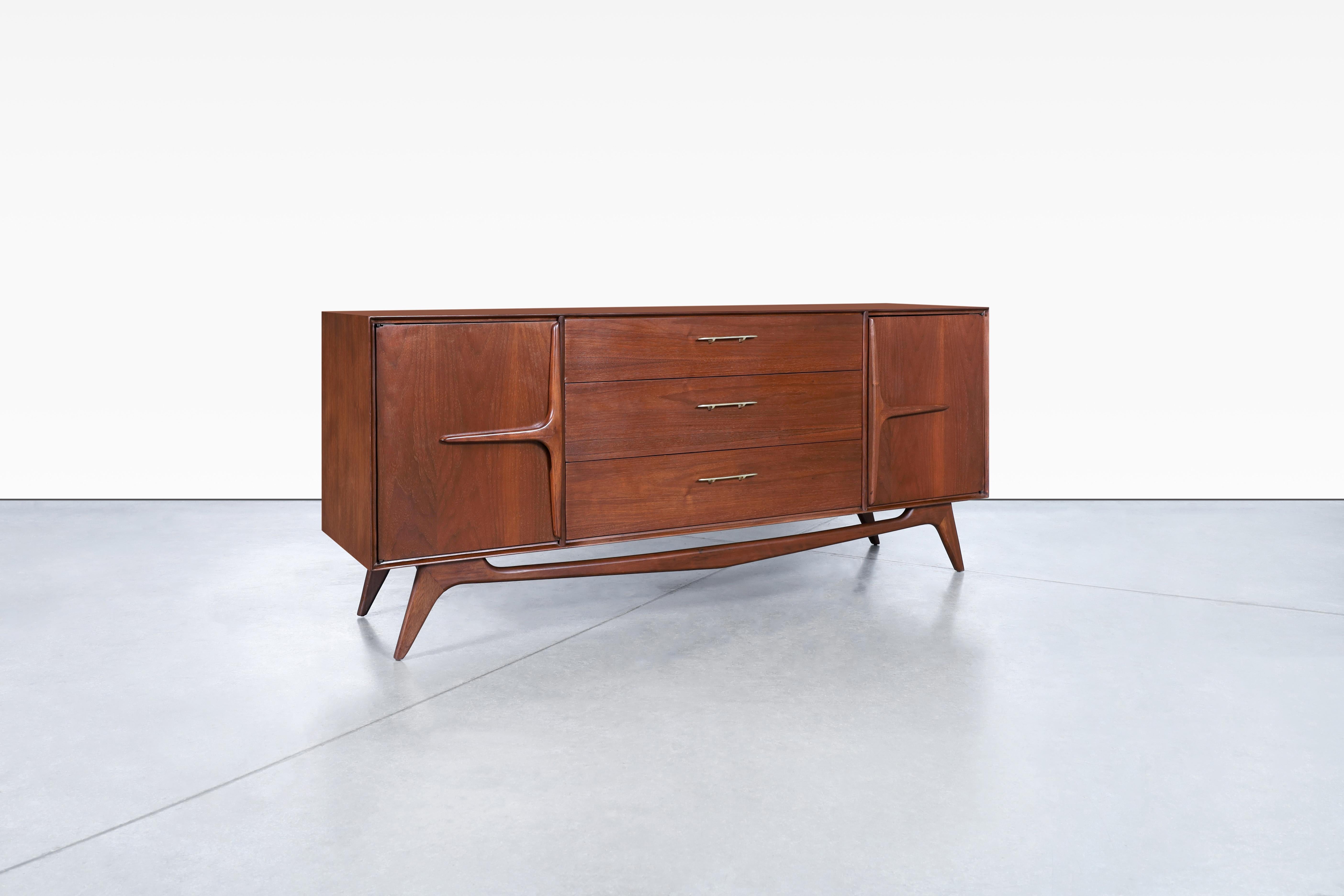 Wonderful mid-century modern sculptural walnut dresser, manufactured in the United States, circa 1950s. This dresser is a masterpiece, crafted from the highest quality walnut wood with a daring design that is bound to catch your eye. The solid brass