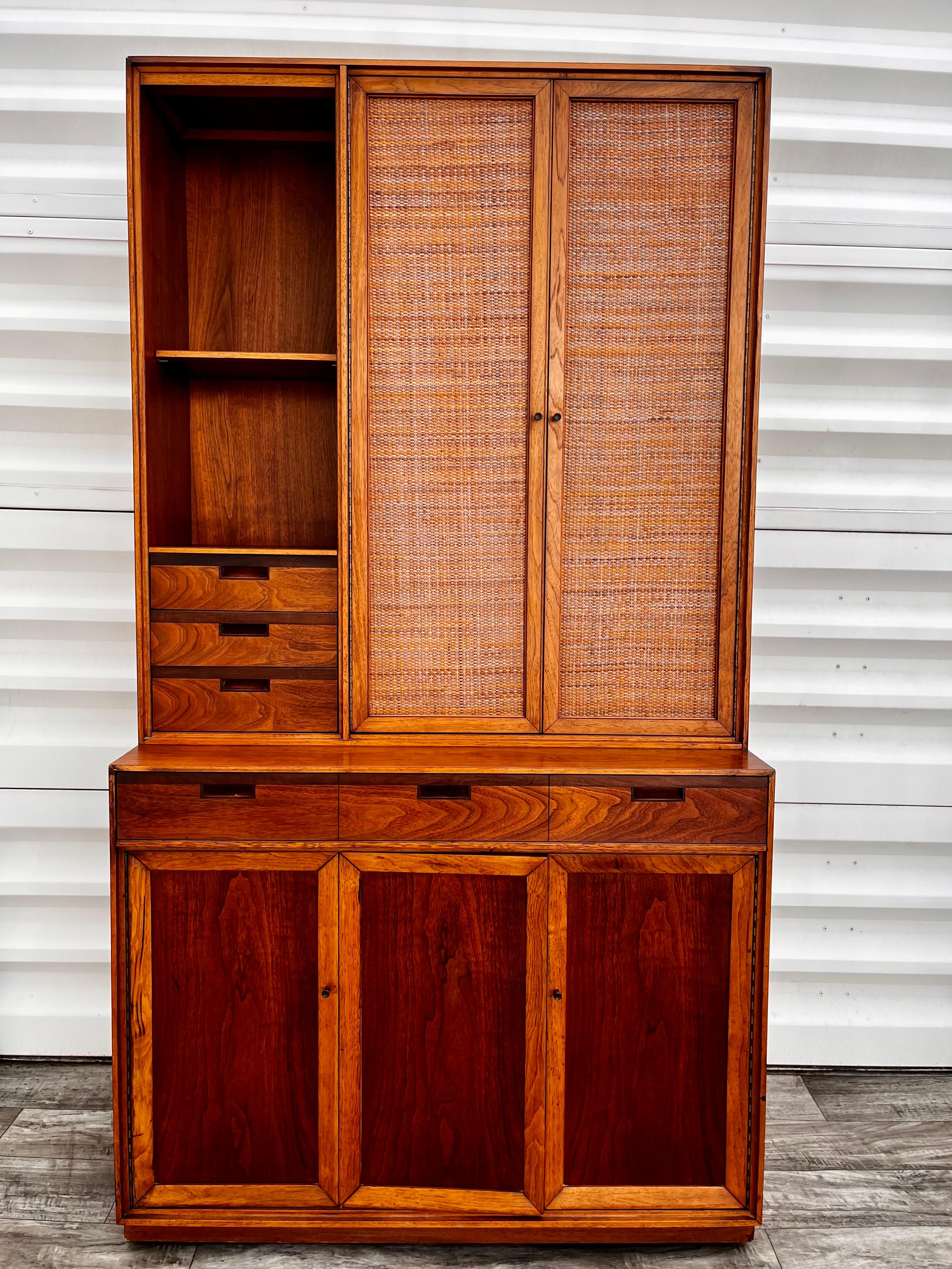 Vintage Mid-Century Modern secretary/ wall unit cabinet in the John Stuart's Janus Collection Style. Circa 1960s
Features a pull-out writing shelve surface hidden by a false front drawer, two top woven cane doors, three small drawers with dovetail