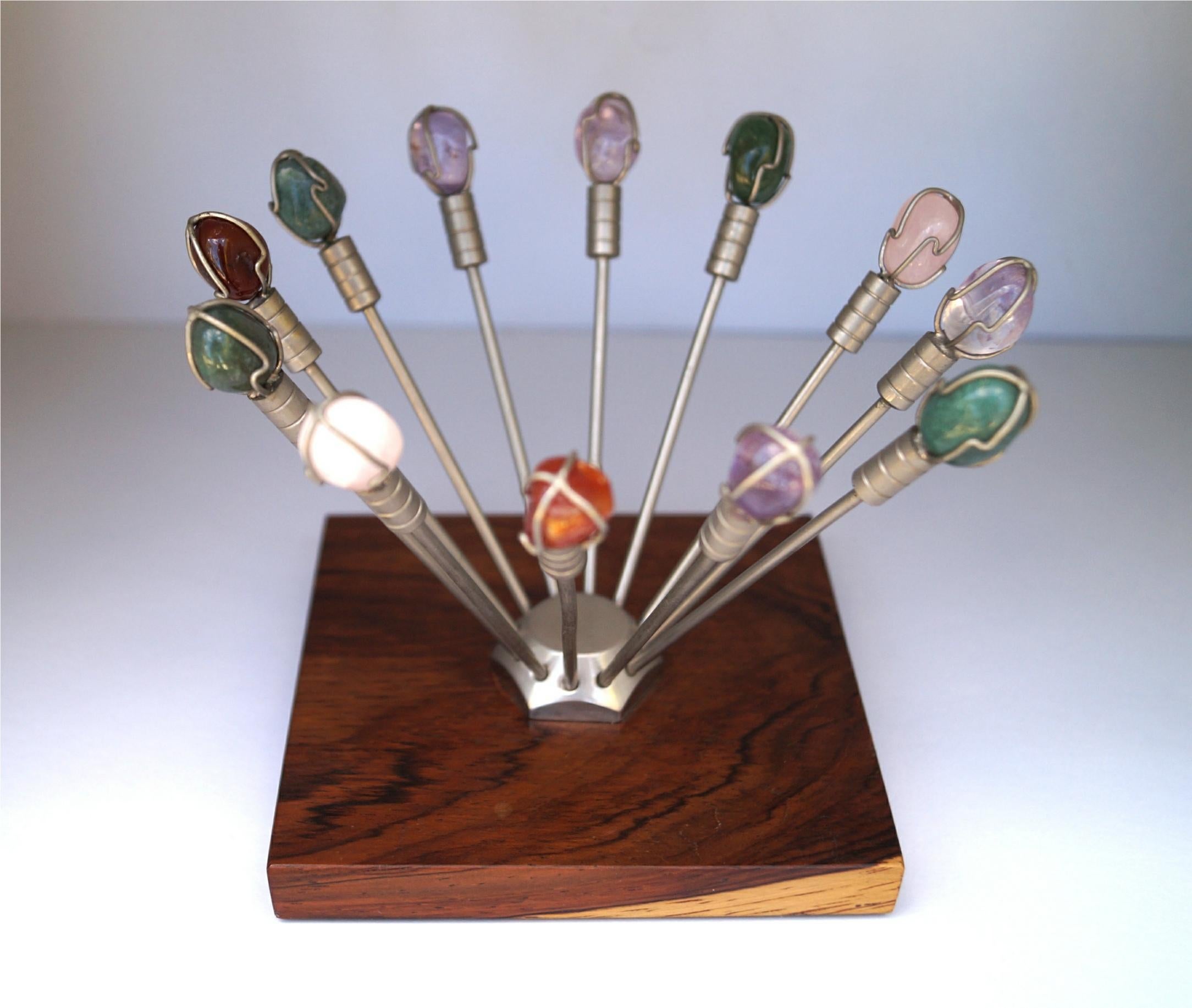This is a unique set of vintage cocktail picks/hors d'oeuvres snack picks with different polished semi-precious stones mounted on the top. Each of the picks are displayed in a wood based stand.

This lovely set is in excellent vintage
